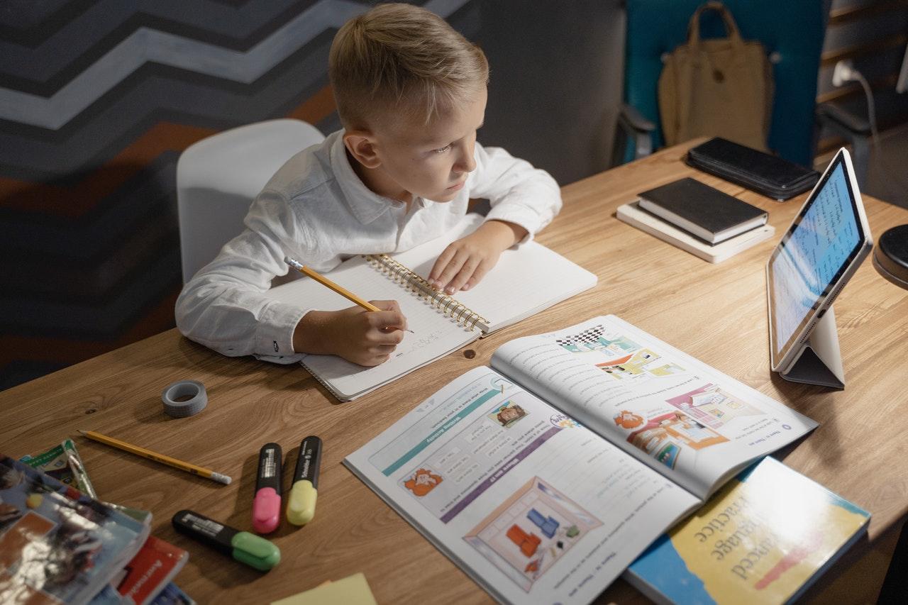 Een jong kind schrijft in schrift kijkende naar een tablet
