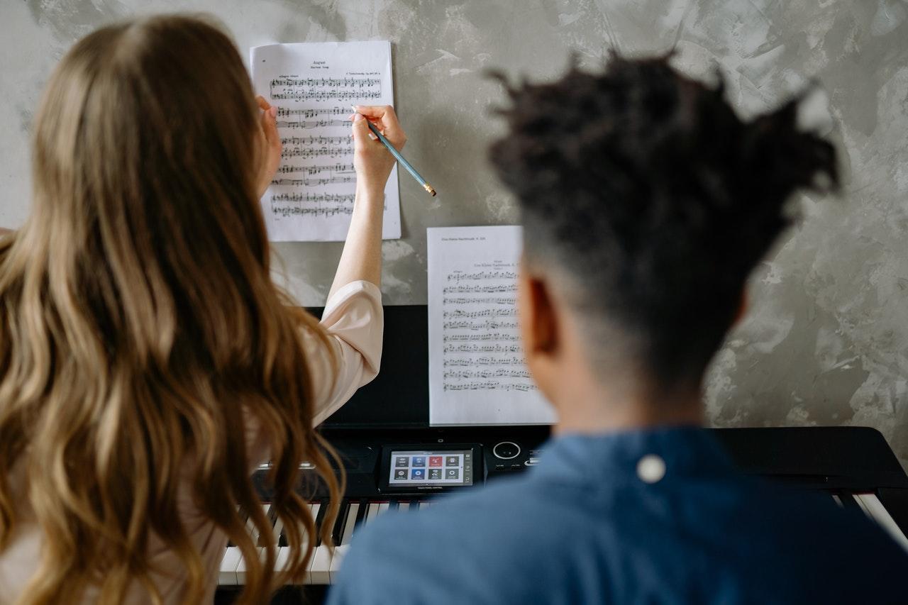 Twee personen achter piano met bladmuziek
