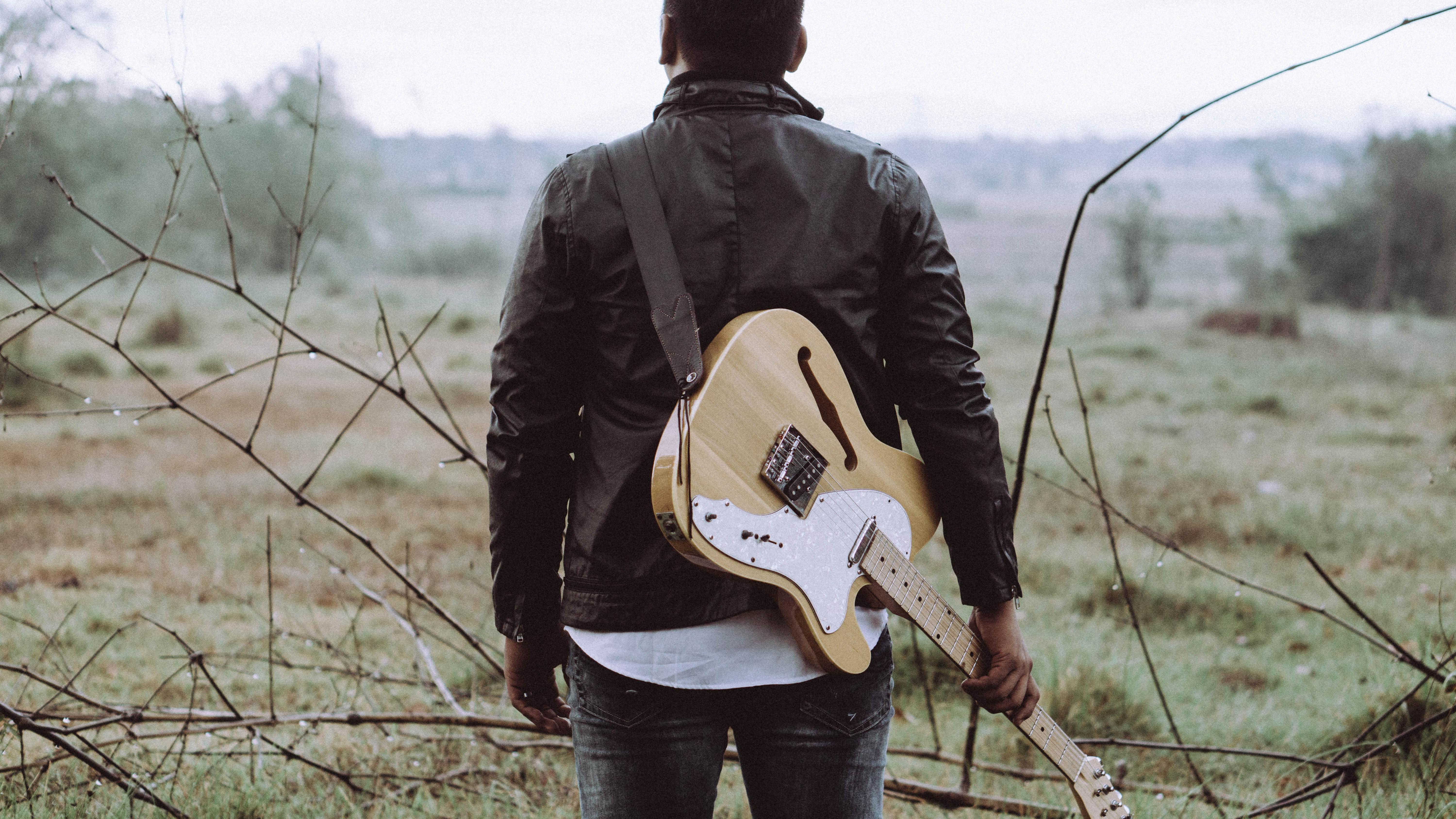 Een man loopt door een veld met een gitaar om zijn schouder gehangen