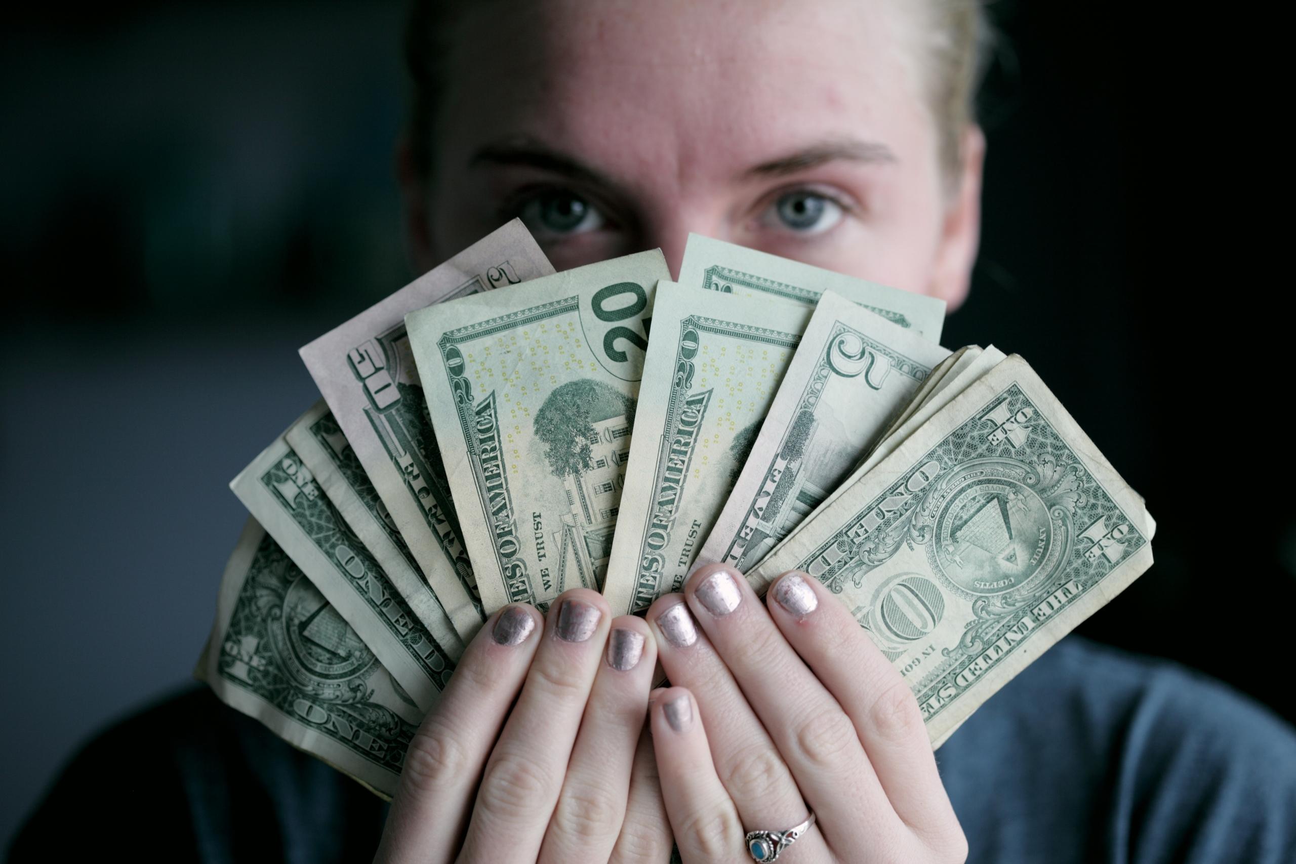 Een vrouw kijkt over een waaier van dollars heen