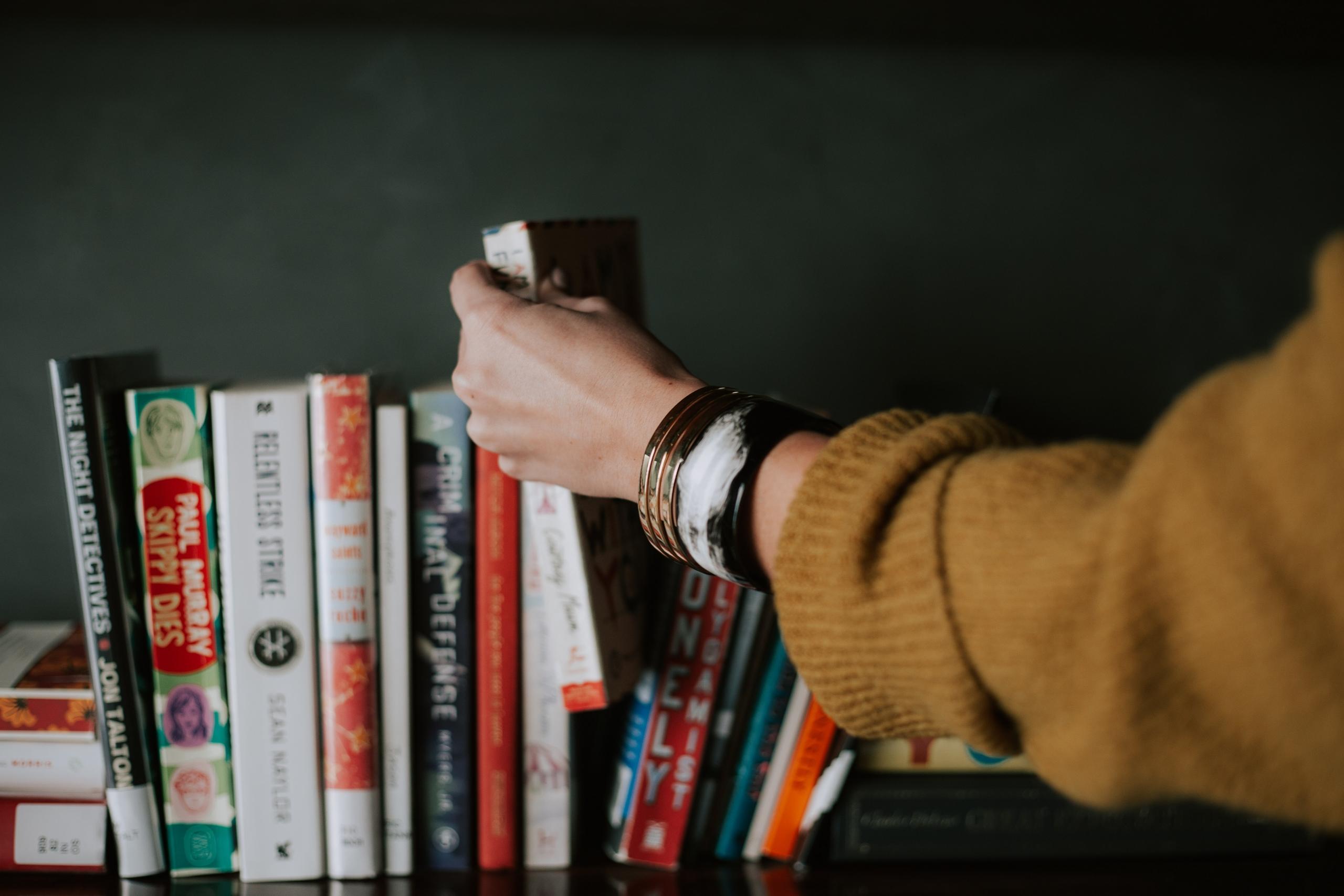 Een persoon kiest een boek uit een boekenkast
