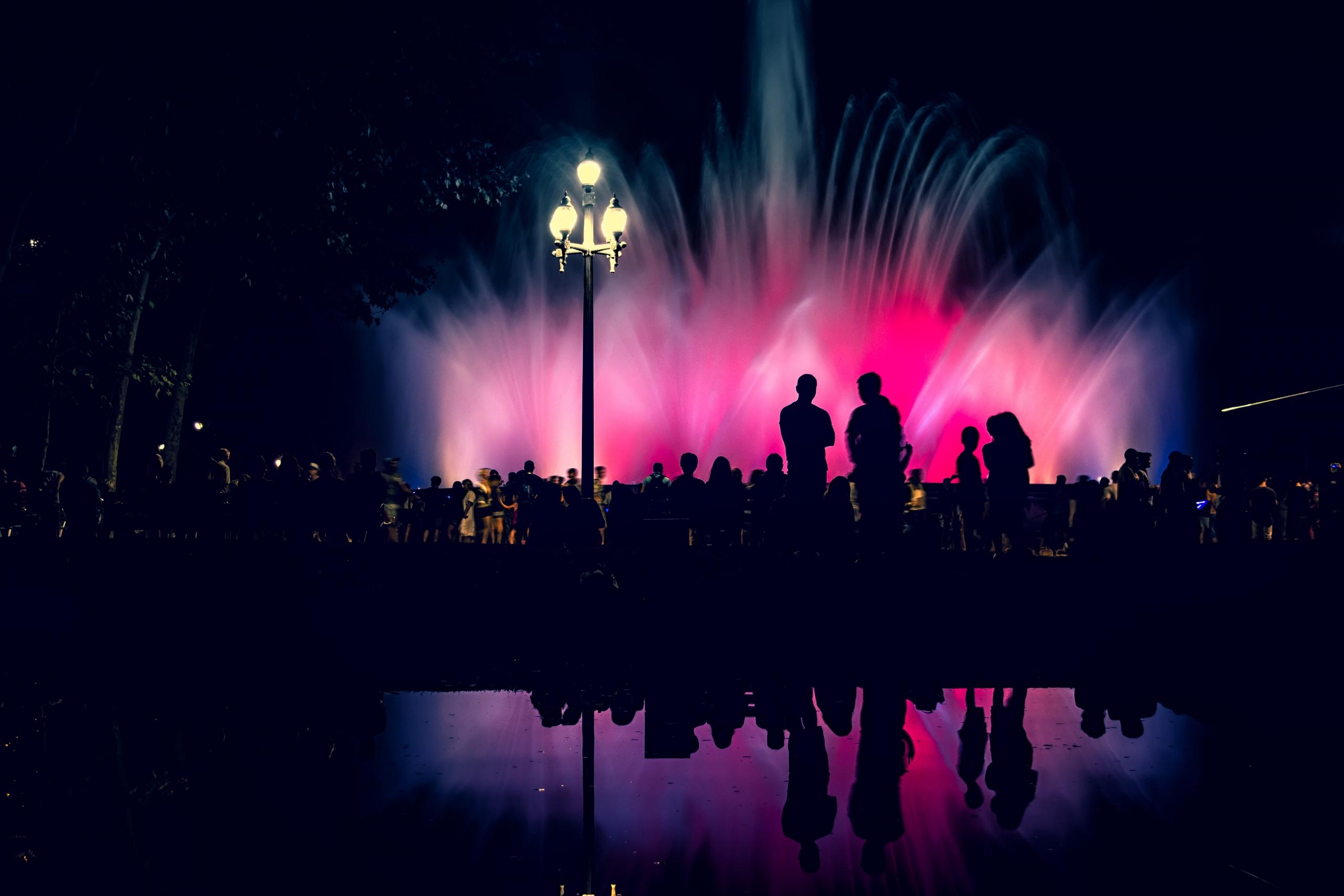 mensen staan in het donker bij een lichtshow met fontein