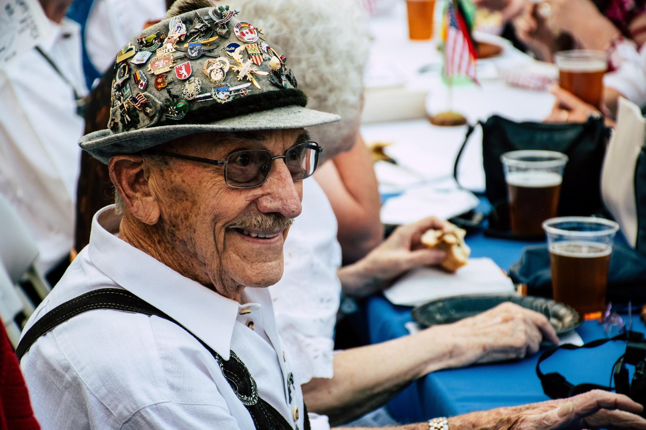 Man met hoed vol speldjes zit aan tafel met bier