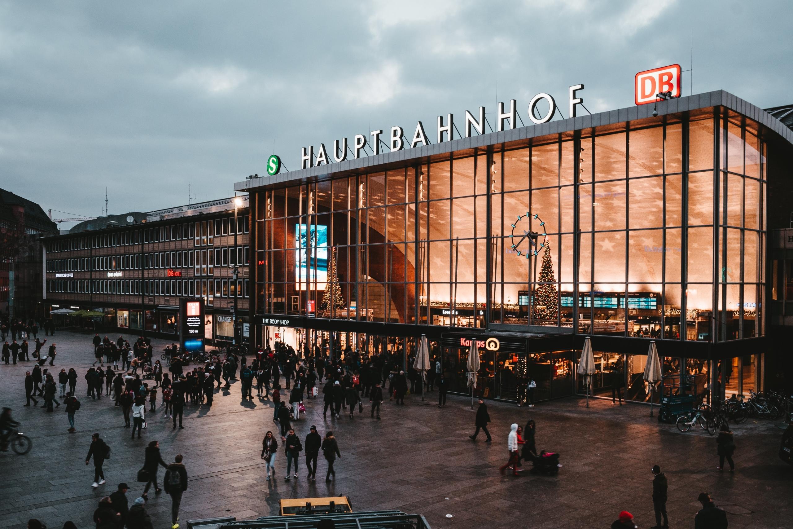 Stationsplein waar mensen lopen met aanzicht op voorgevel