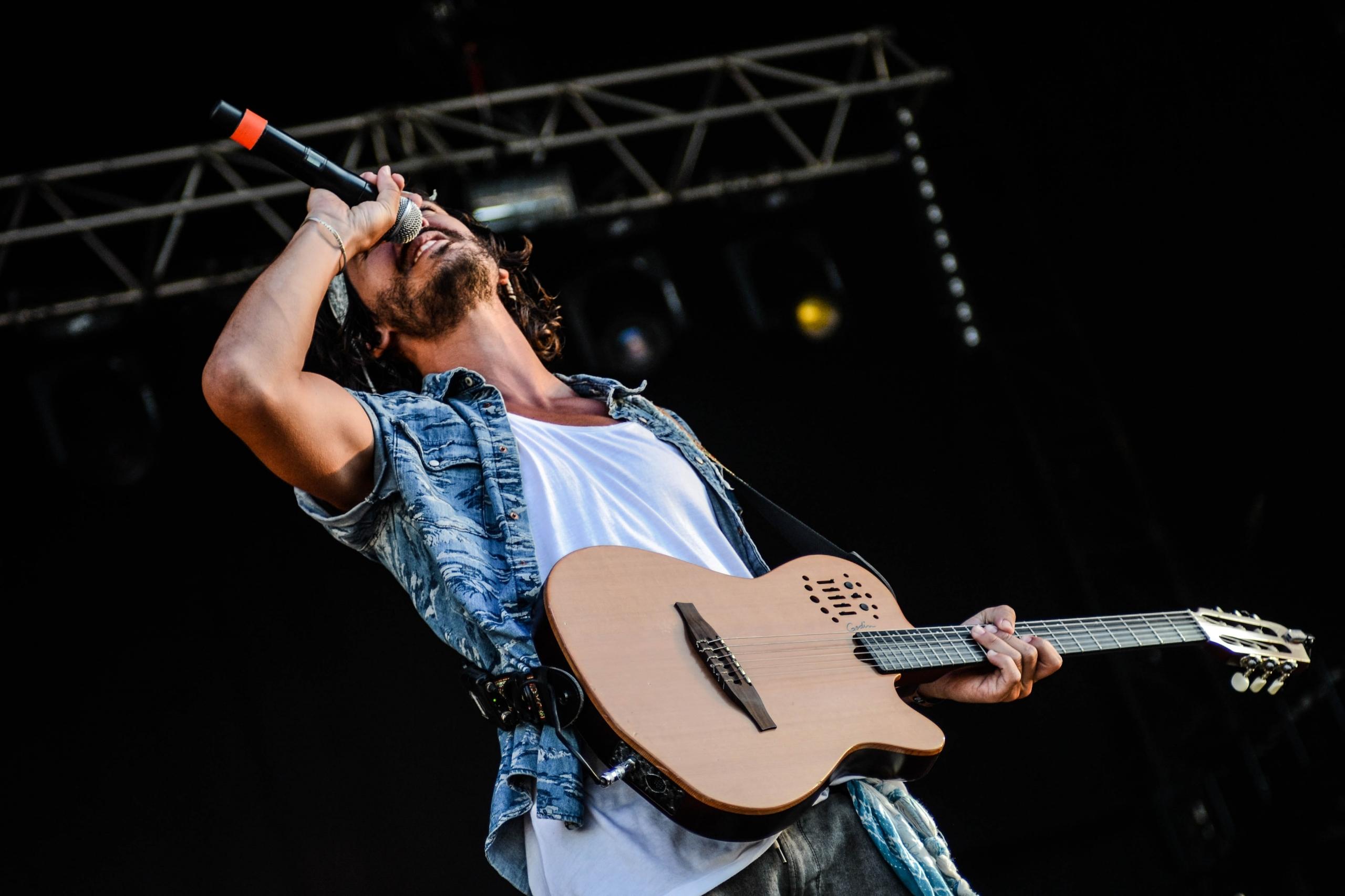 Man zingt op een podium in een microfoon met gitaar om zijn nek.