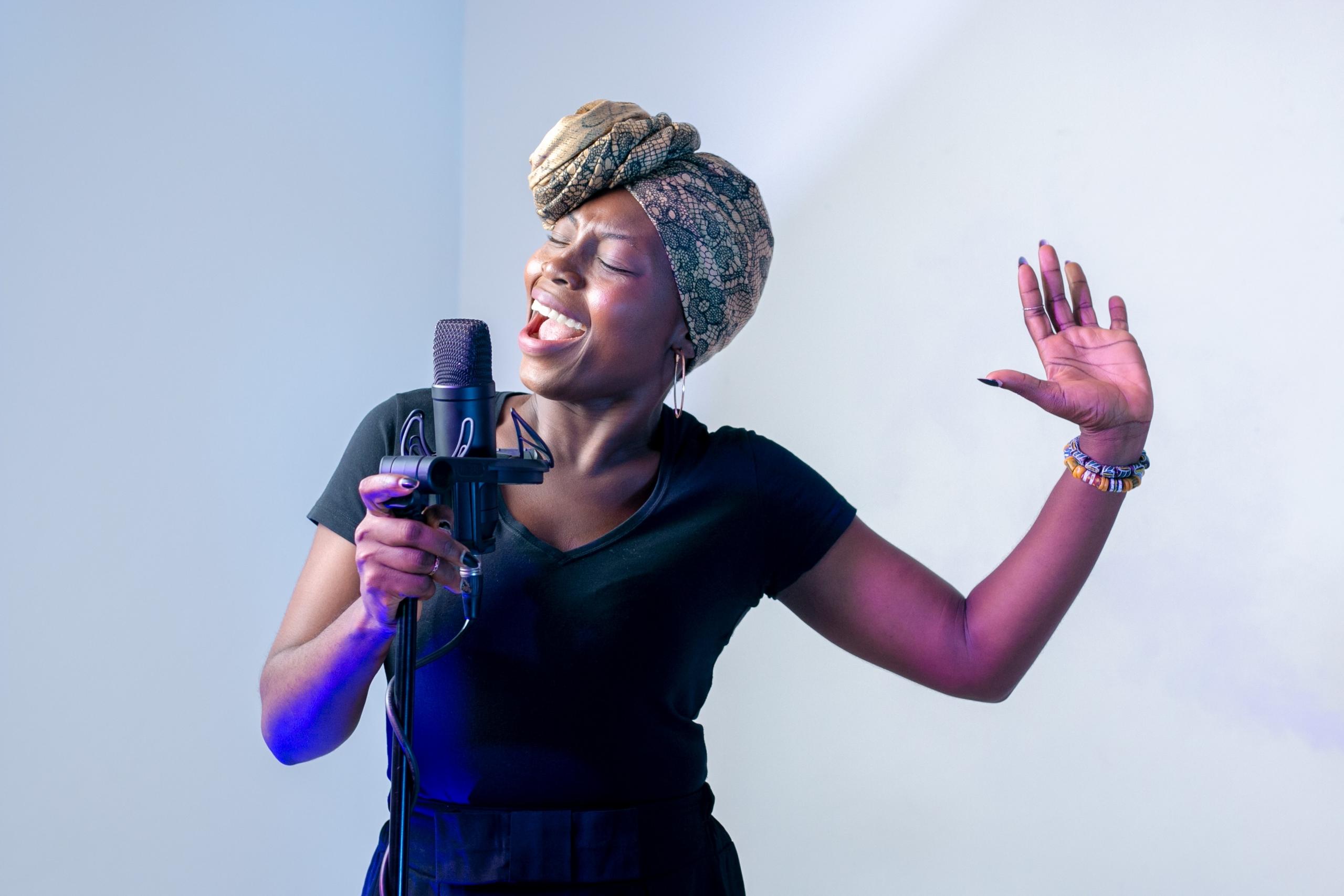 Vrouw met hoofddoek om zingt in een microfoon die in een standaard is geplaatst.