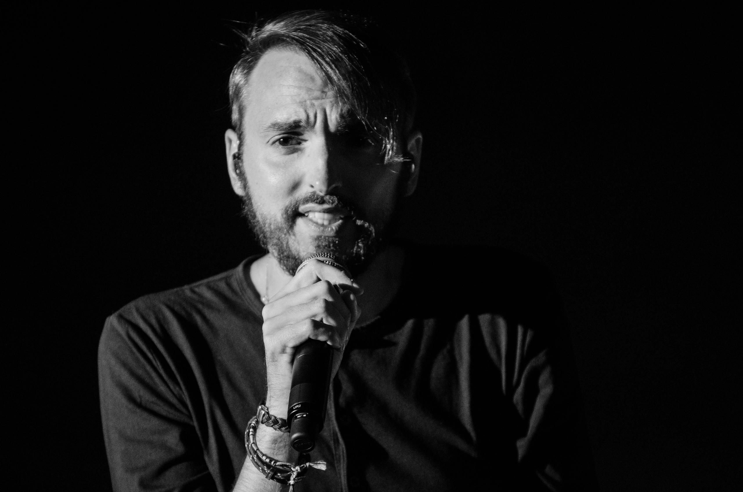Man zingt in een microfoon en kijkt direct de camera in.