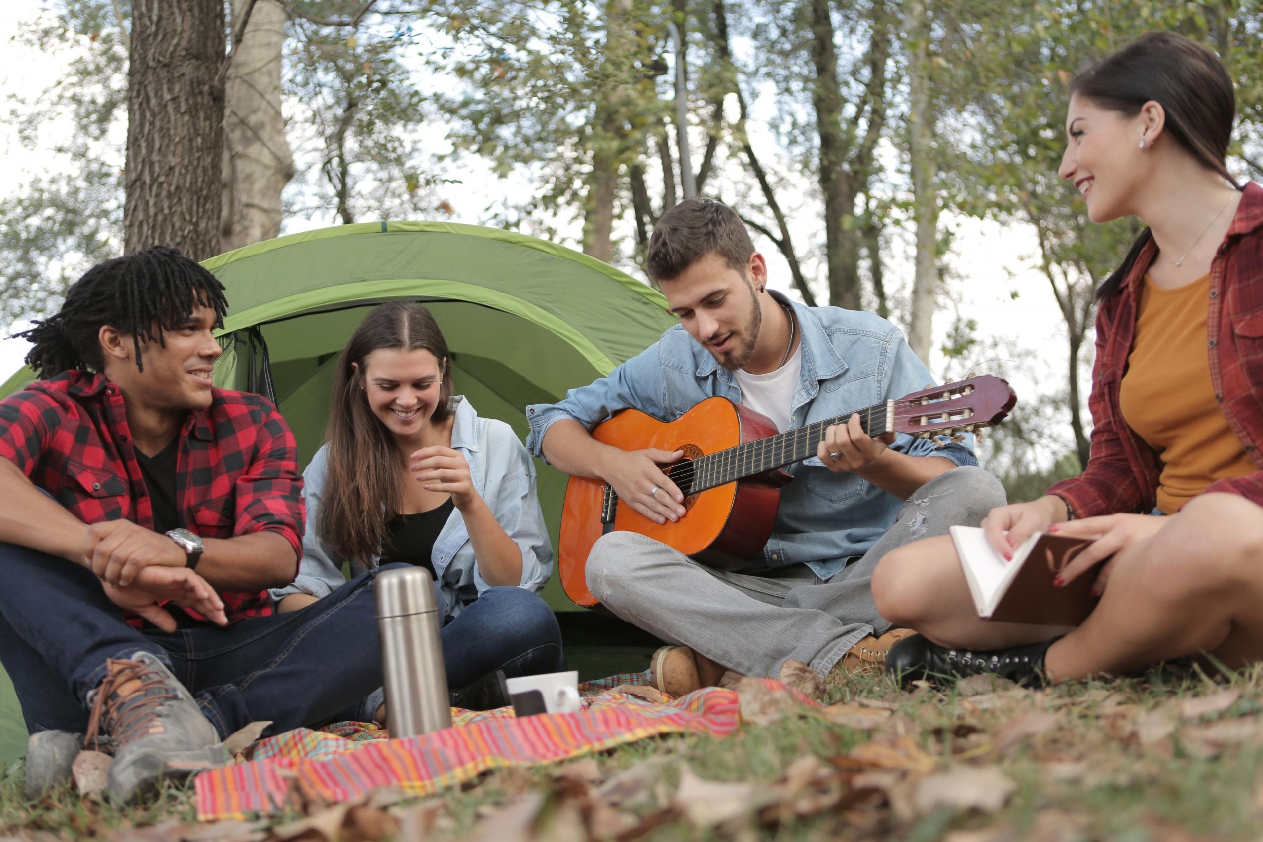 Groep jongeren zingen in een kring in het bos met gitaar.