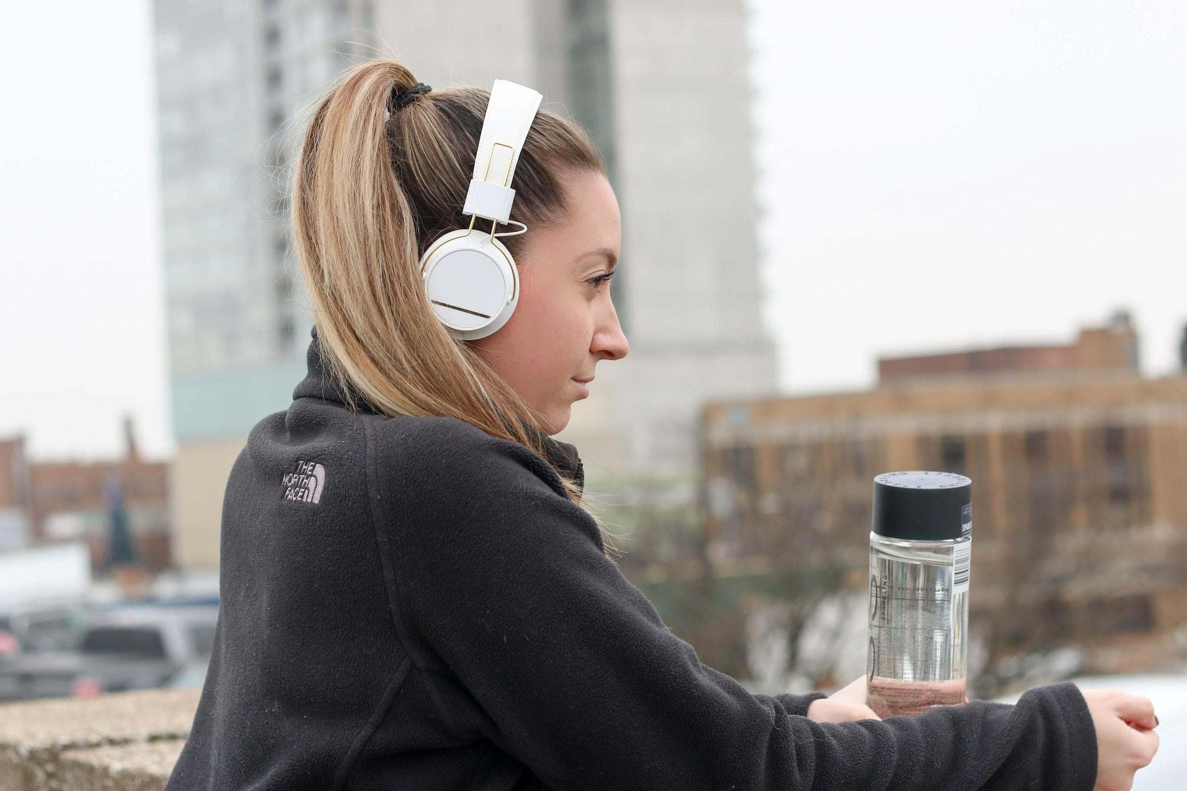 Vrouw buiten met witte koptelefoon op en fles water in hand