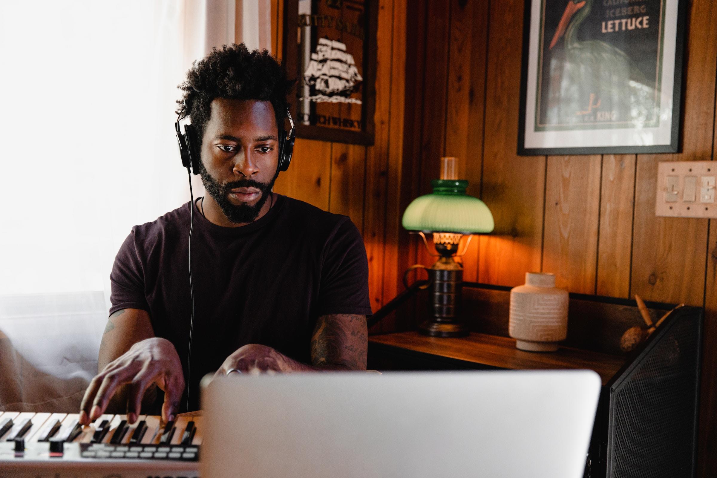 Man met koptelefoon achter piano en laptop.
