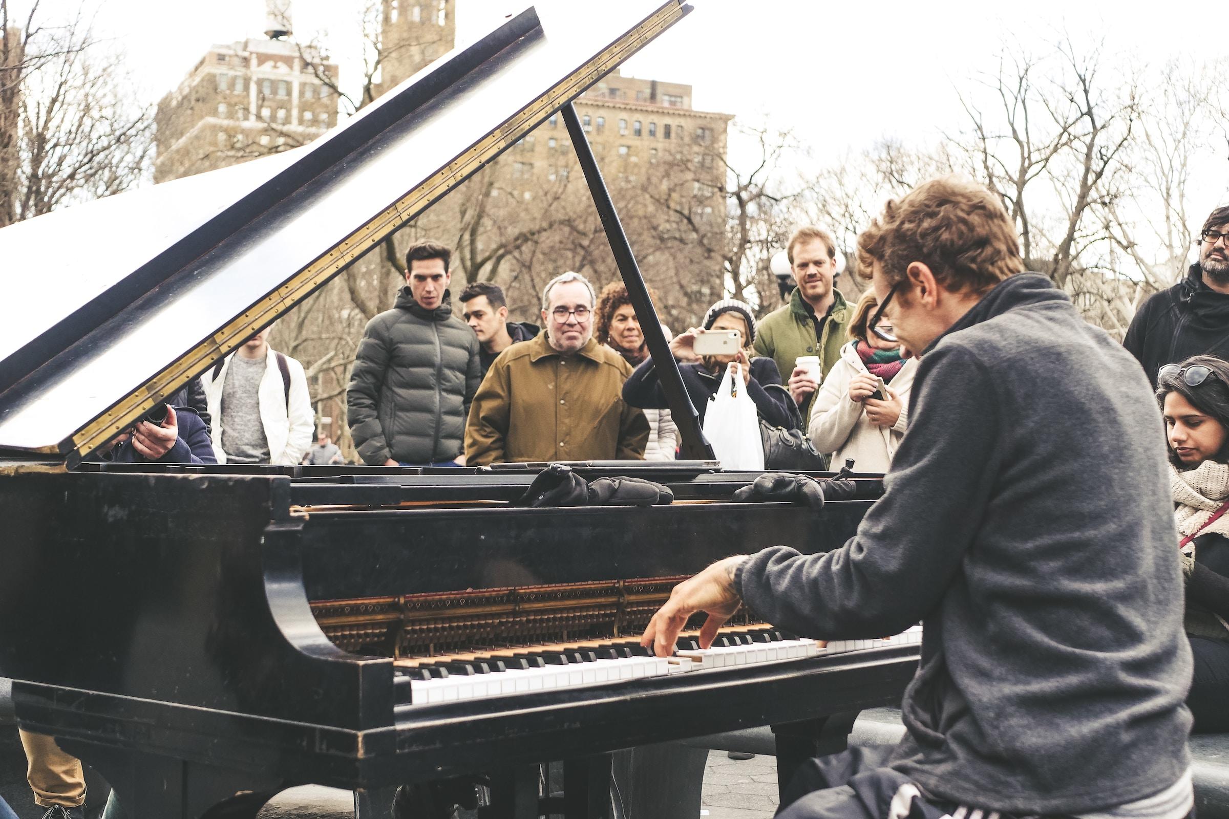 Man buiten achter piano met publiek