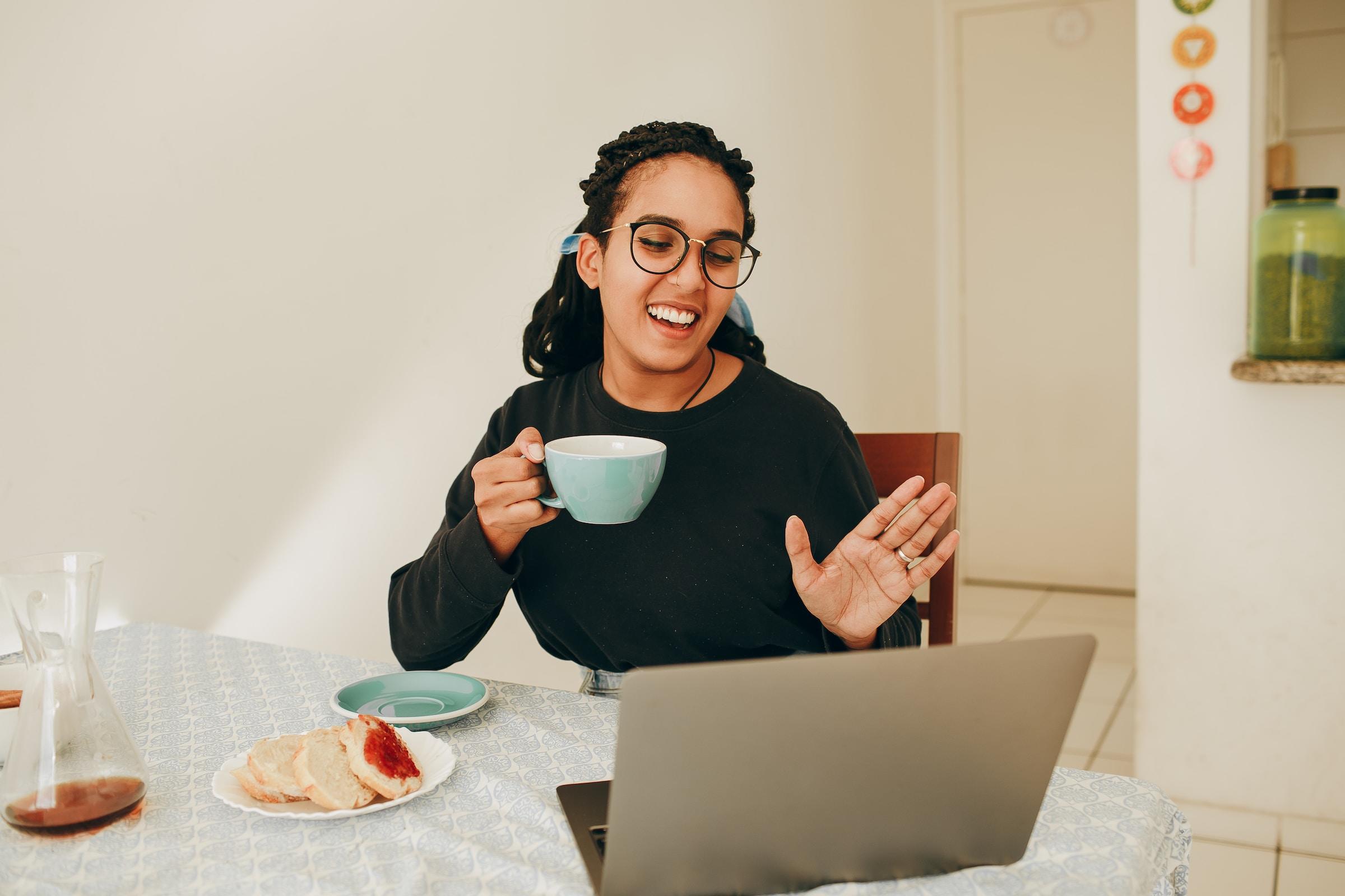 Vrouw met kop in de hand die iemand begroet op haar laptop