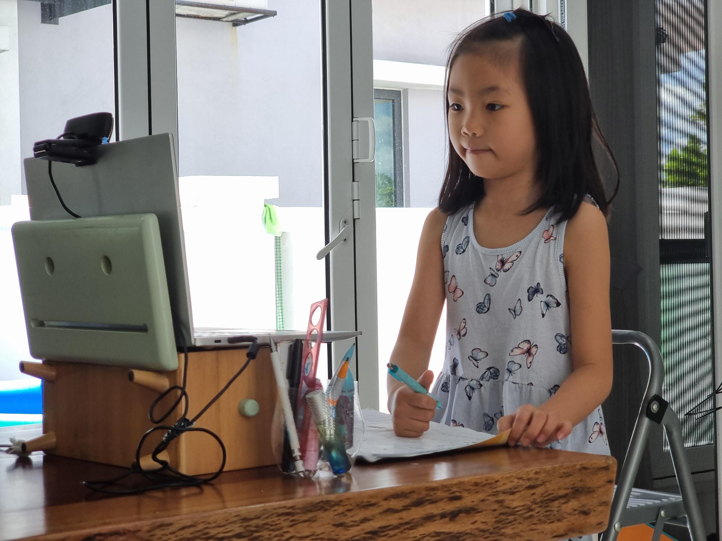 Staand kind met pen kijkend naar laptop