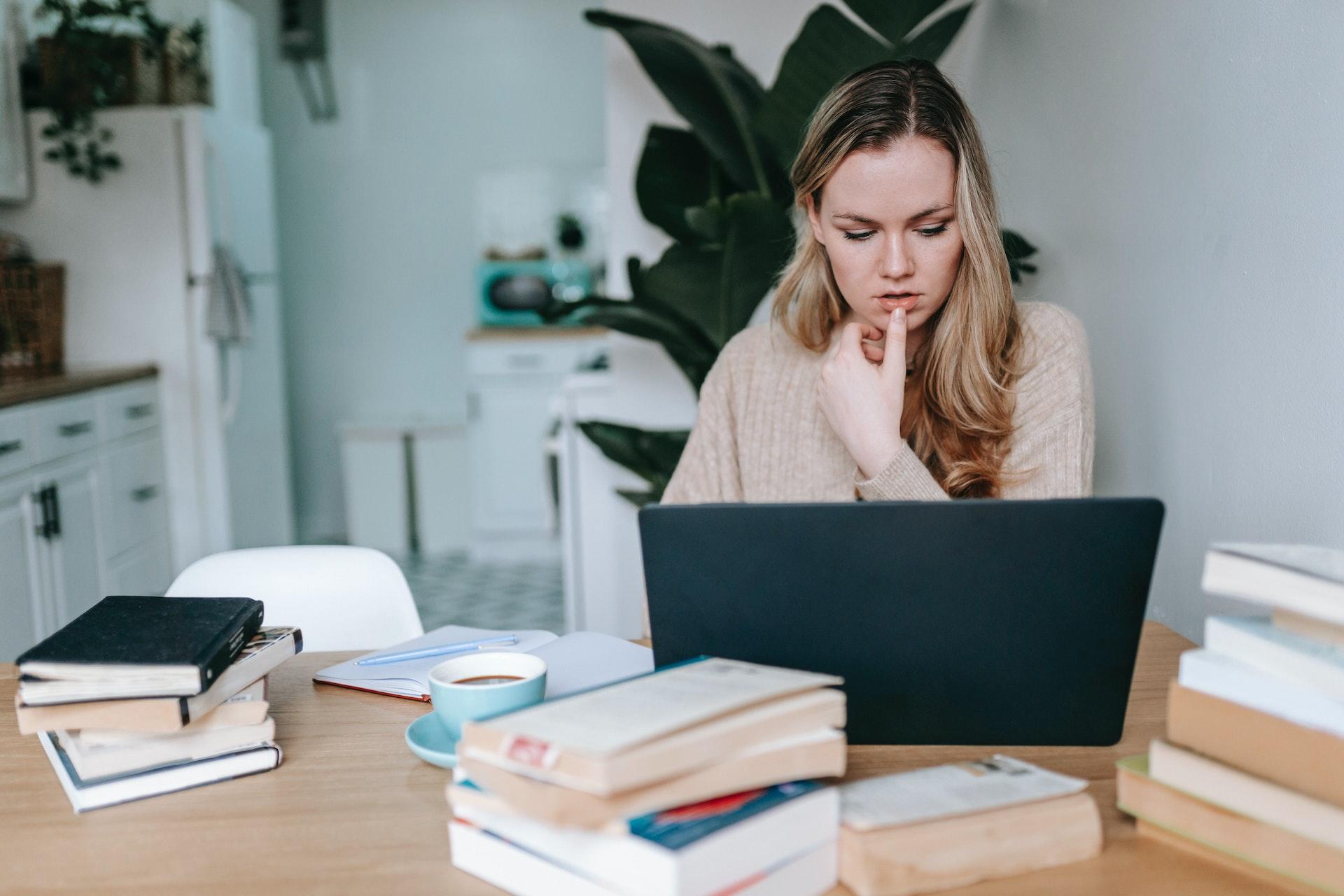 vrouw studeert op haar laptop naast boeken over Spaanse grammatica