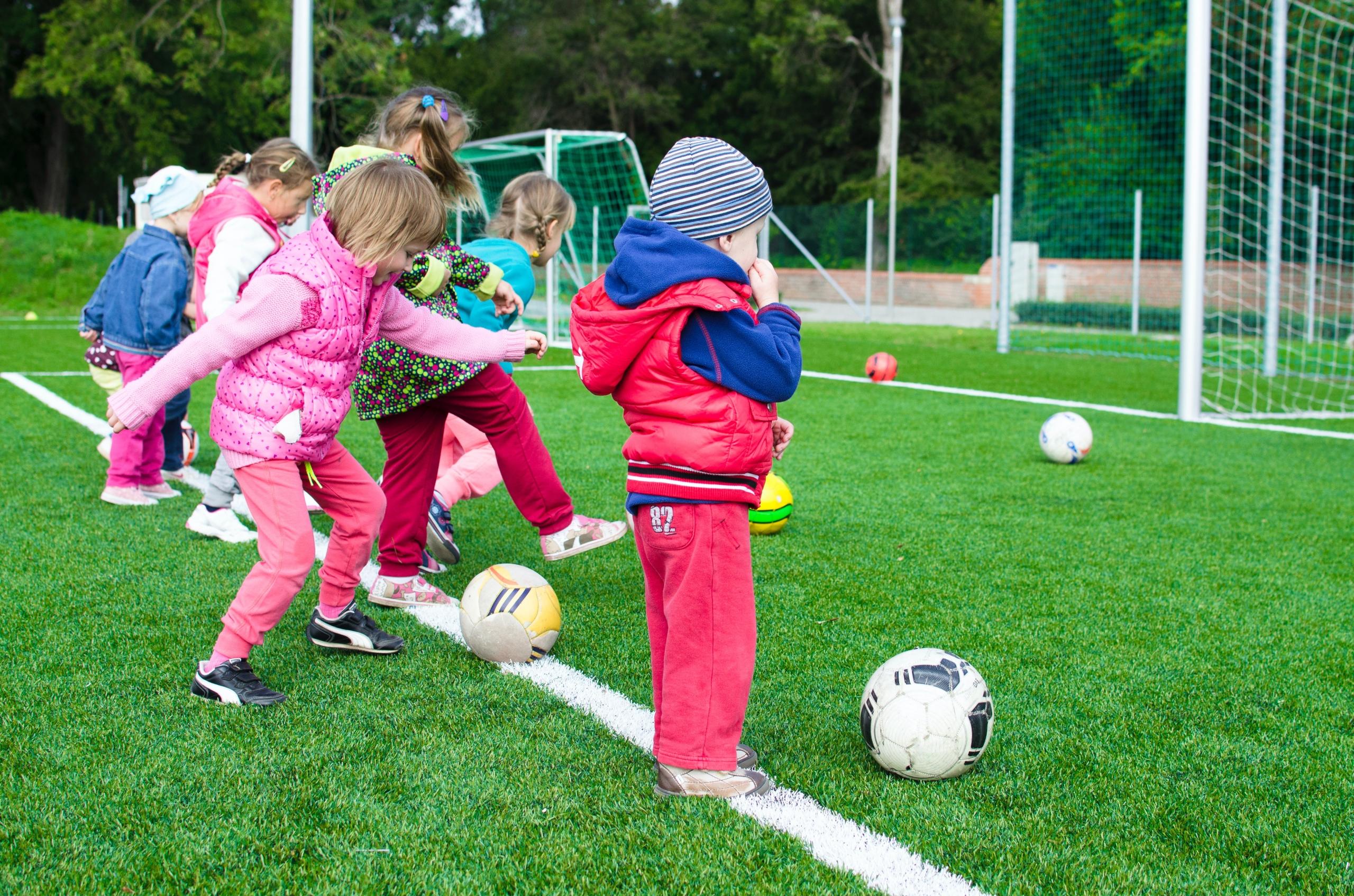 Jonge kinderen staan op een voetbalveld met een bal voor zich.