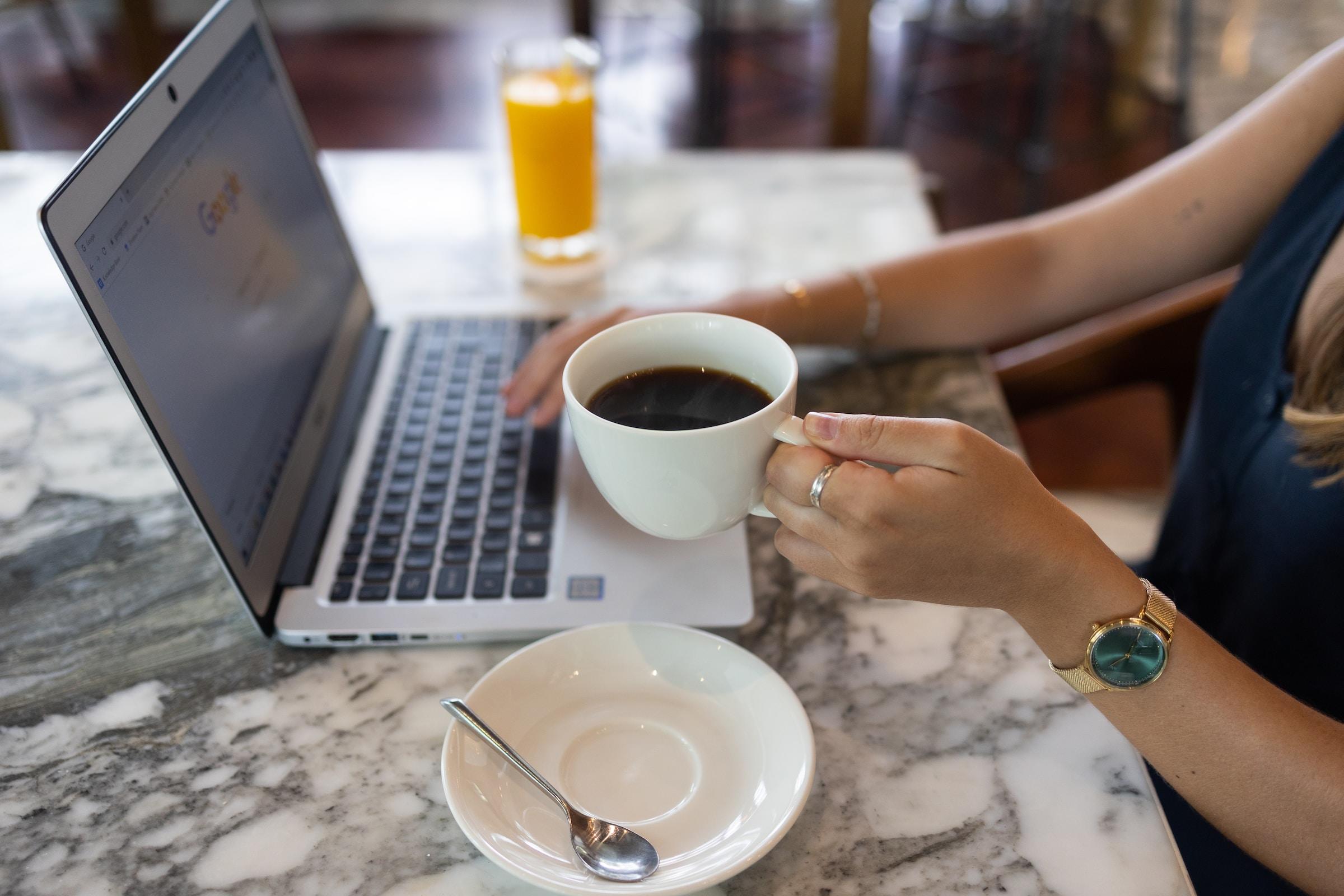 Persoon met koffie achter laptop