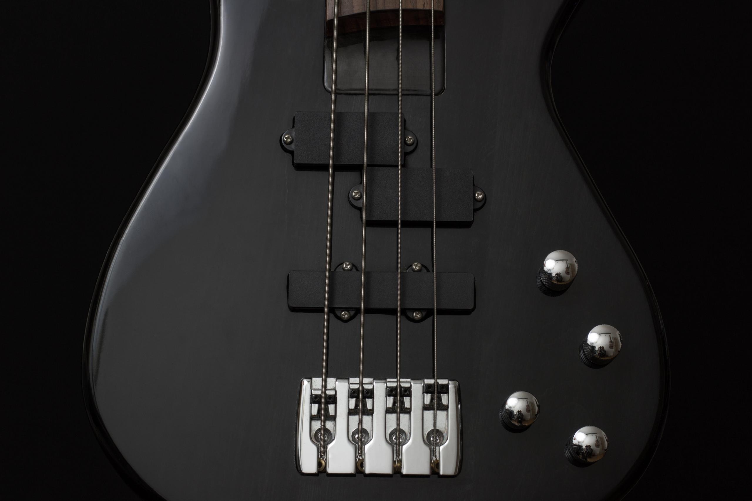 Een close-up van de body van een zwarte basgitaar met de snaren, pickups en regelknoppen zichtbaar.