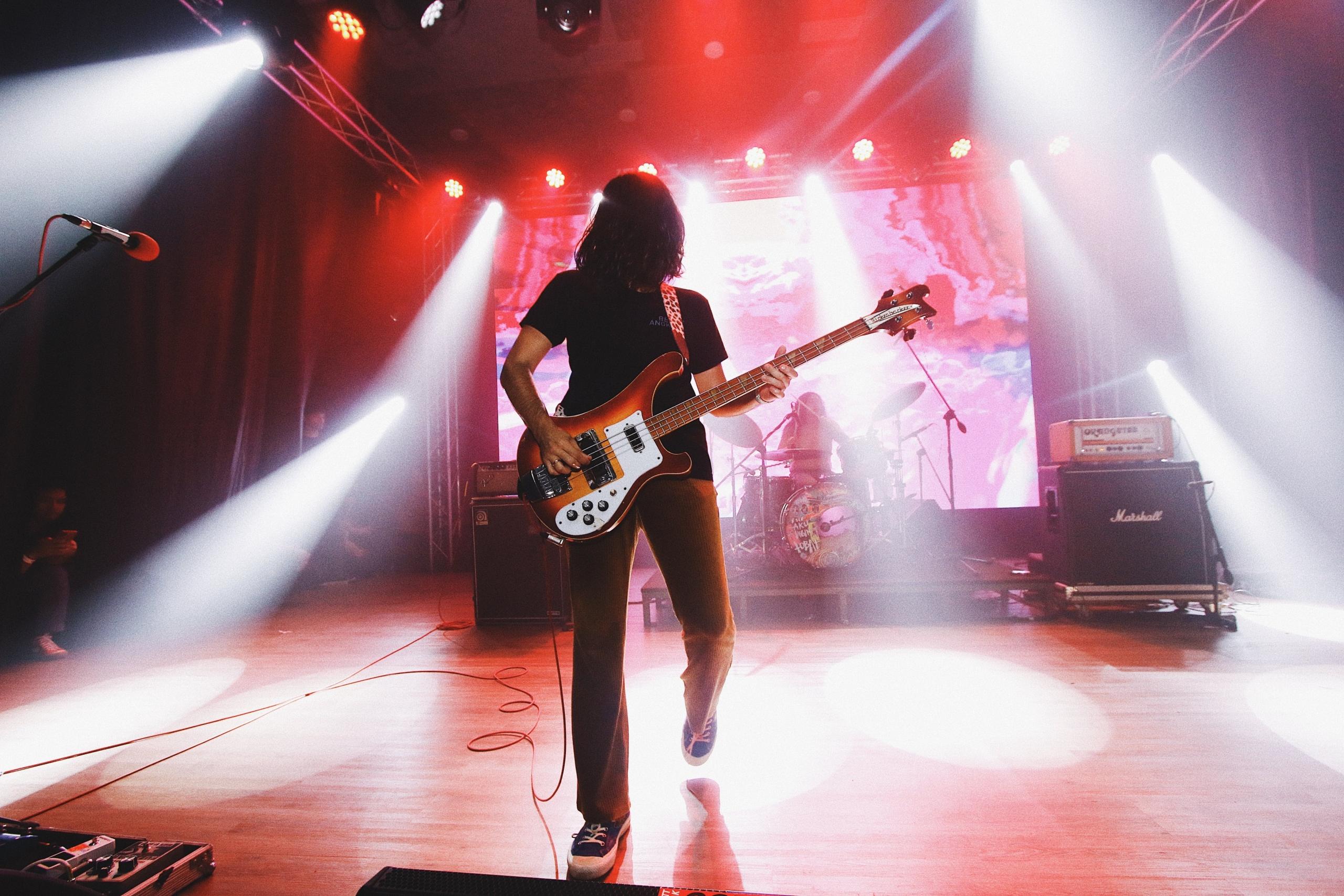 Een bassist staat op een podium met lichtstralen op de achtergrond.
