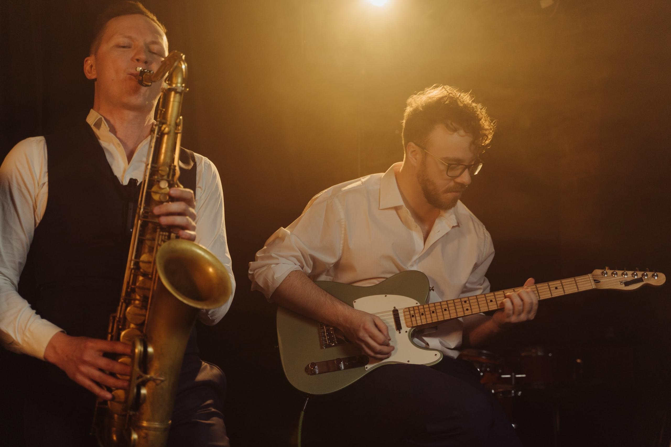Een saxofonist en gitarist spelen samen in een verlichte ruimte.