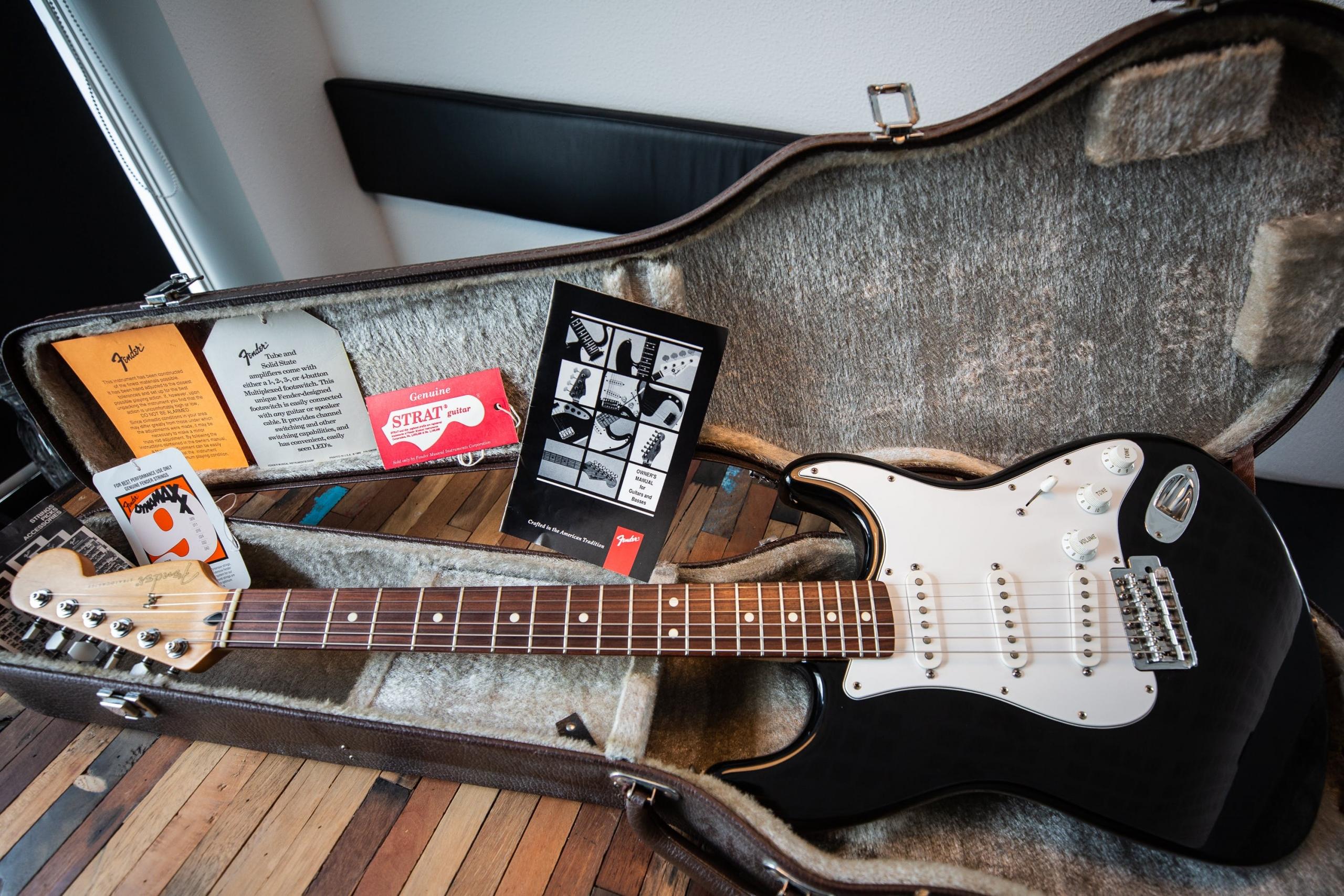 Een elektrische gitaar in een koffer, omringd door diverse muzikale accessoires en boekjes.