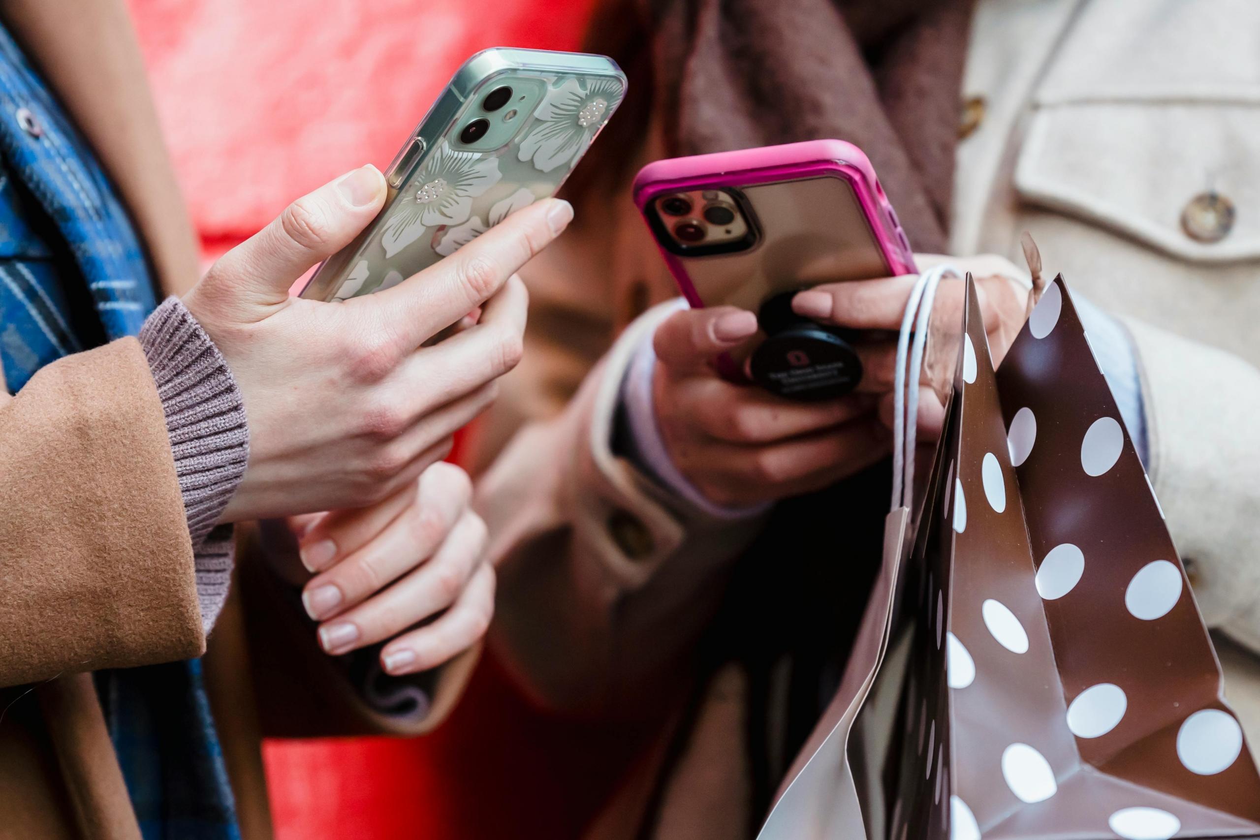 Twee personen houden smartphones vast met kleurrijke hoesjes terwijl ze winkeltassen vasthouden.