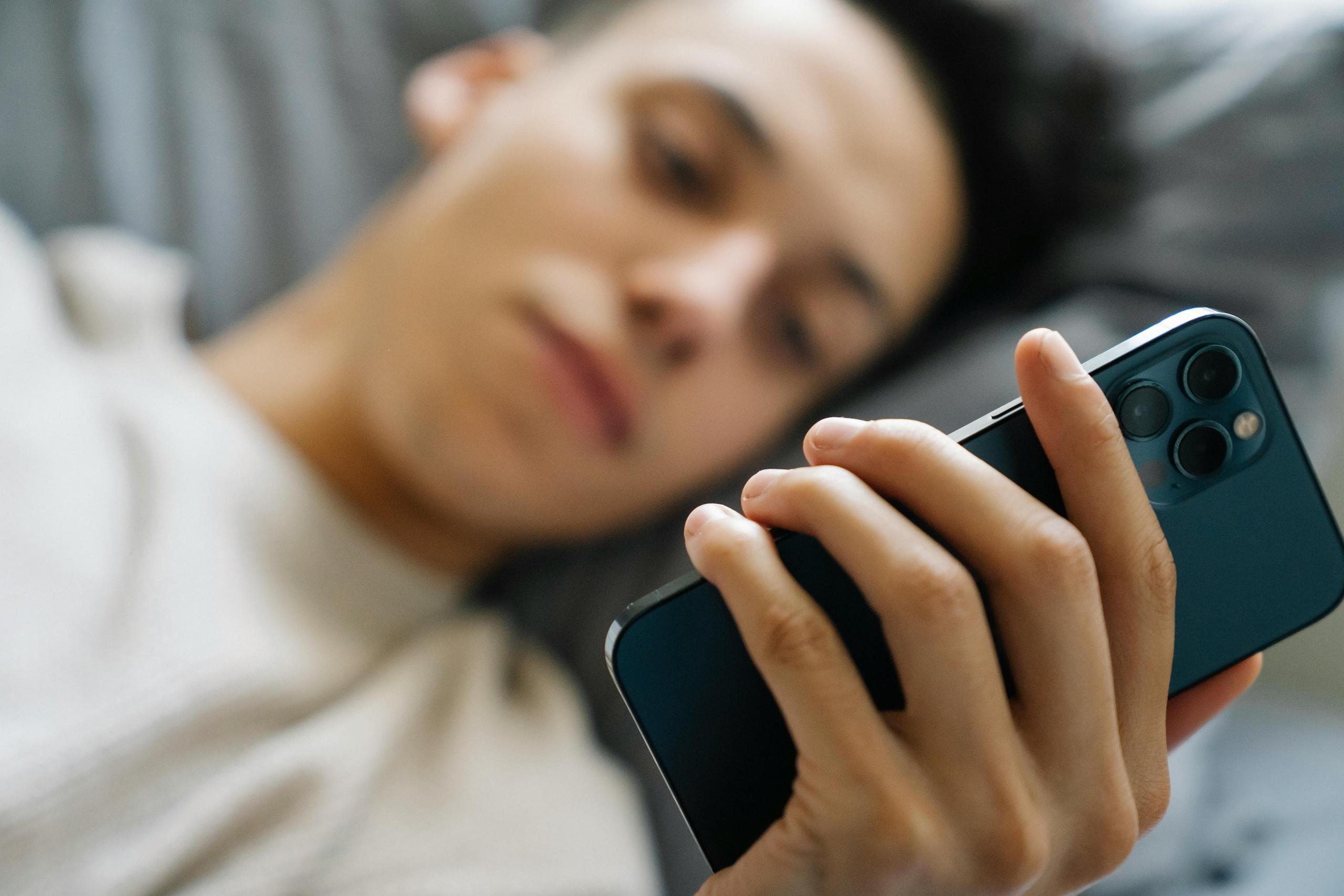 Een liggend persoon, kijkt naar een smartphone in zijn hand.