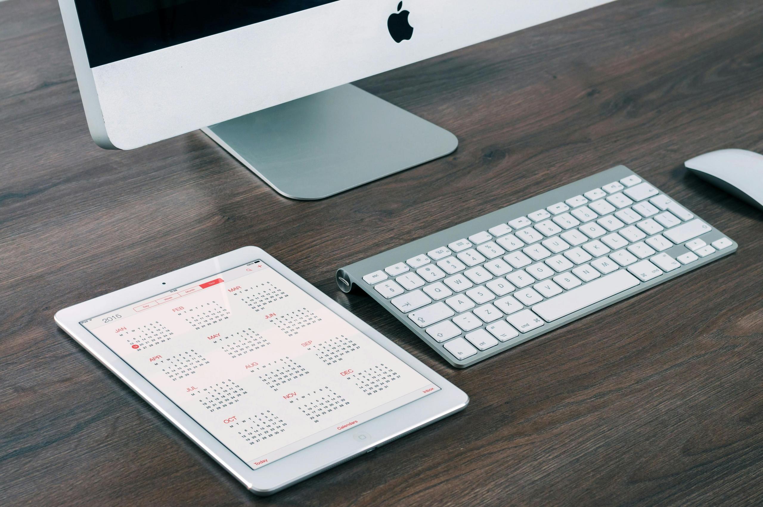 Een iPad met een kalenderapp naast een iMac en toetsenbord.