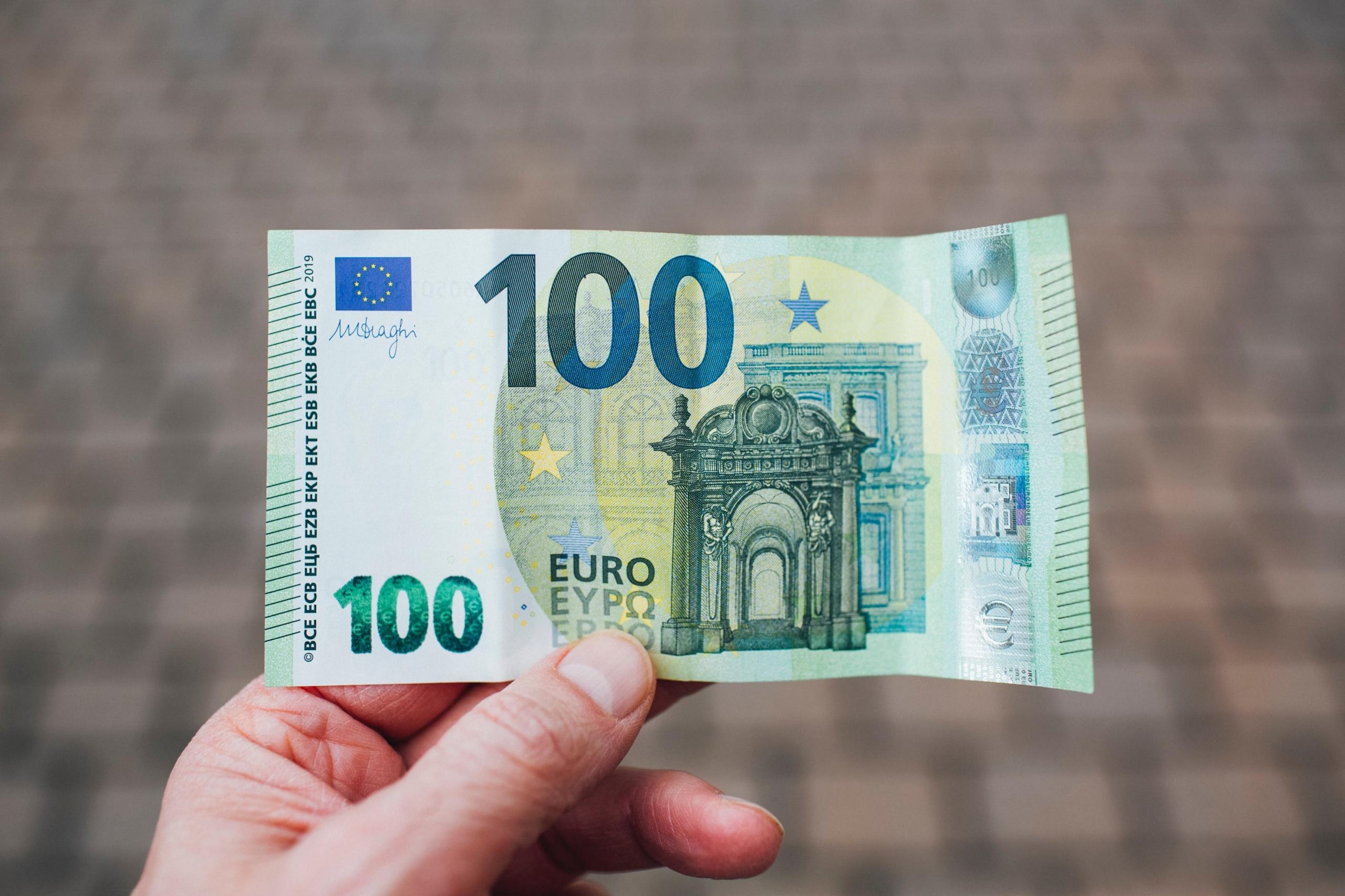 Een honderd eurobiljet wordt vastgehouden tegen een achtergrond.