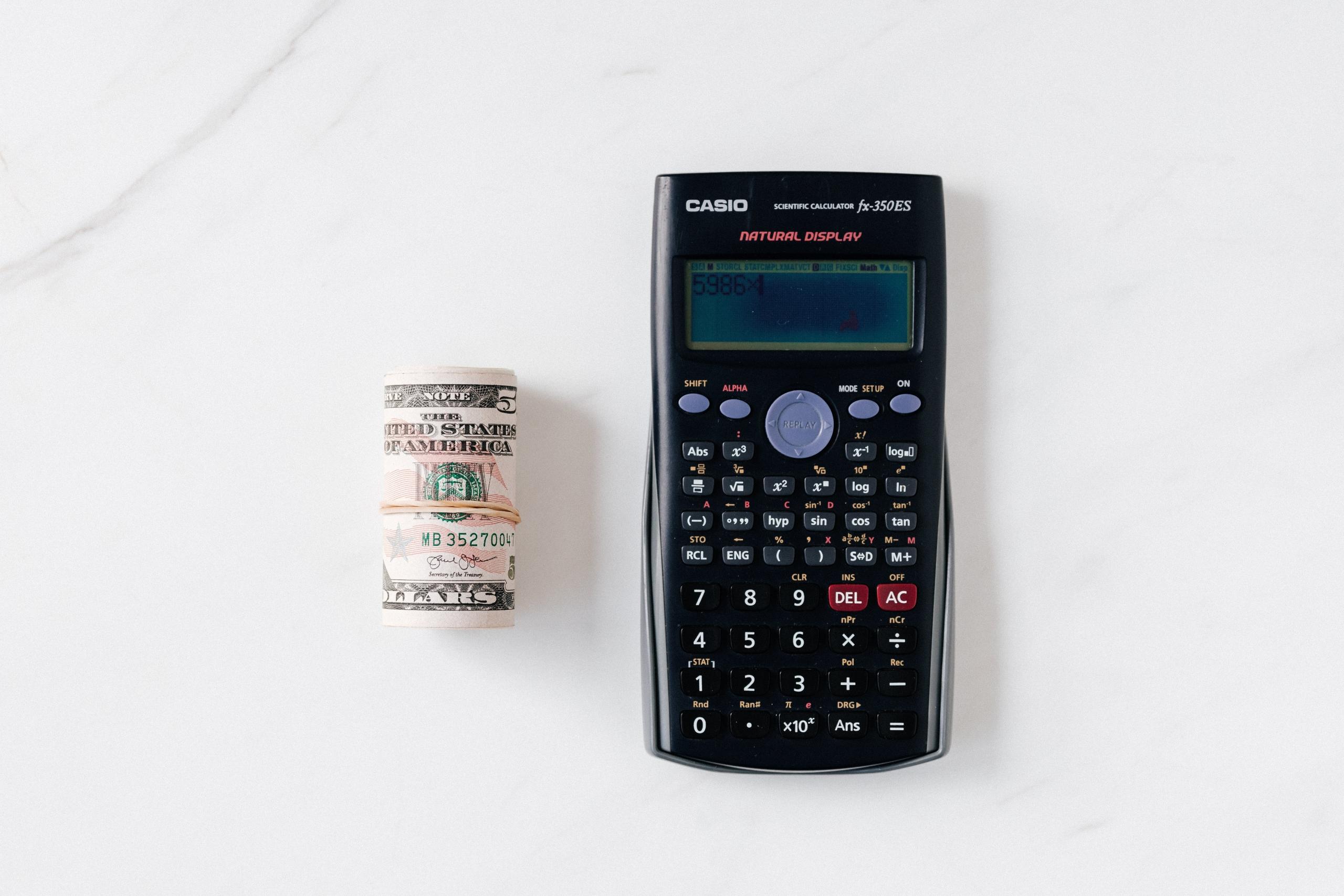 Een opgerolde bundel van vijf-dollarbiljetten naast een Casio rekenmachine.