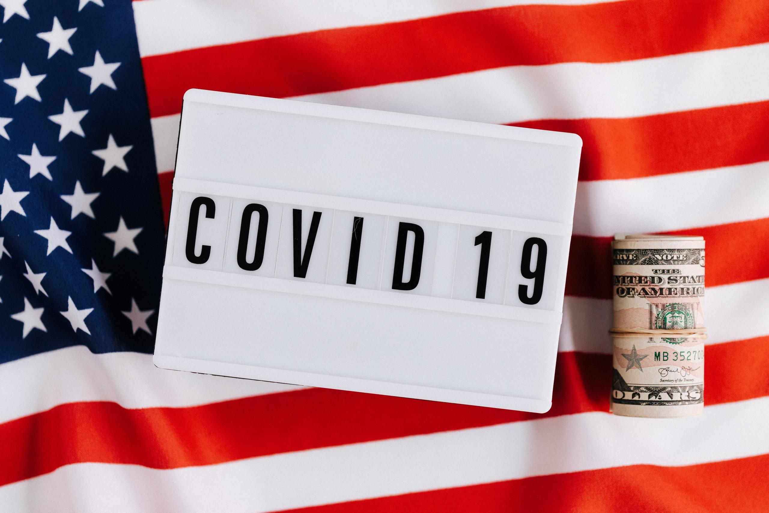 Een bord met "COVID 19" voor een Amerikaanse vlag met een rol dollarbiljetten.