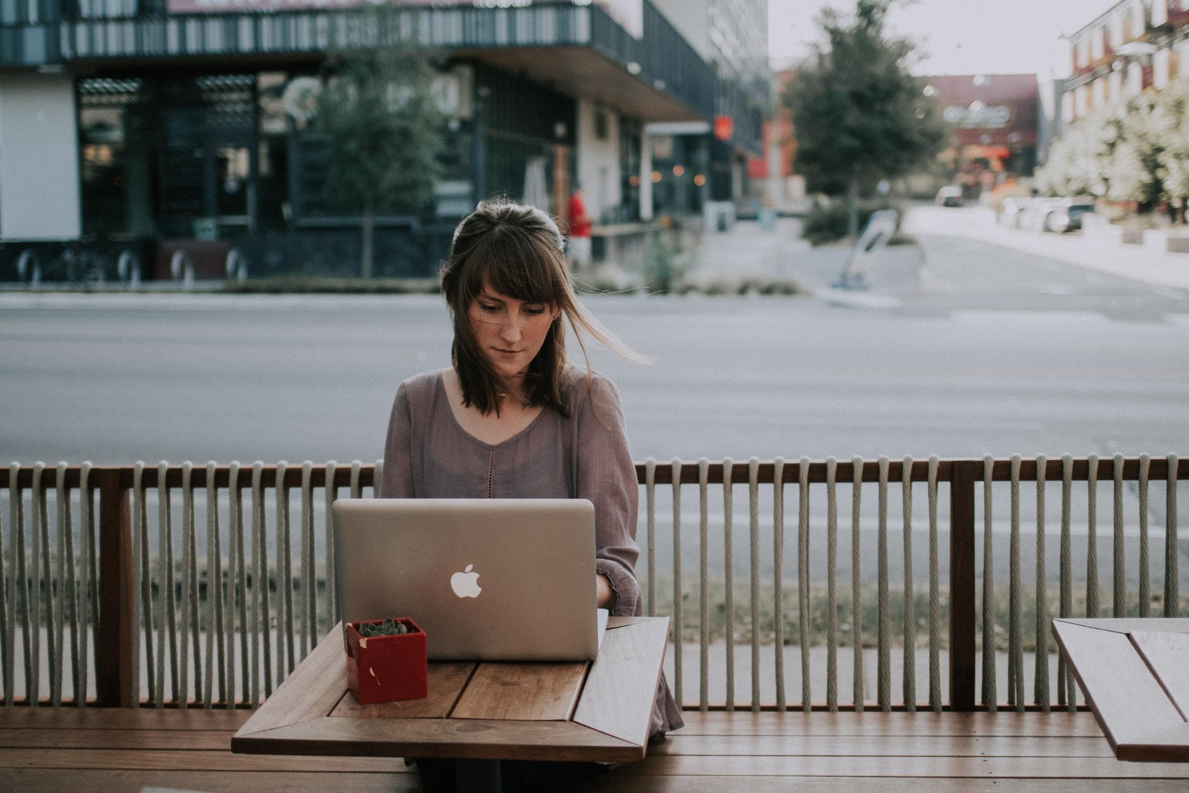 Vrouw buiten aan tafeltje op terras achter laptop