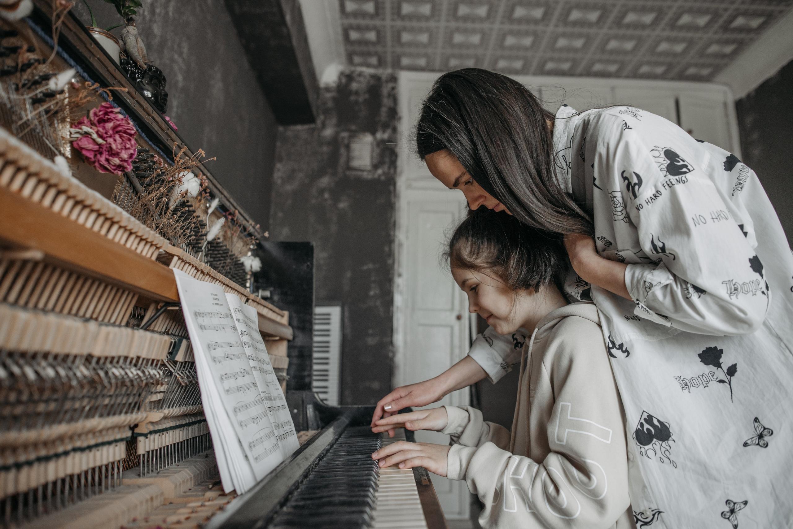 Vrouw en kind zitten samen te spelen op een piano.