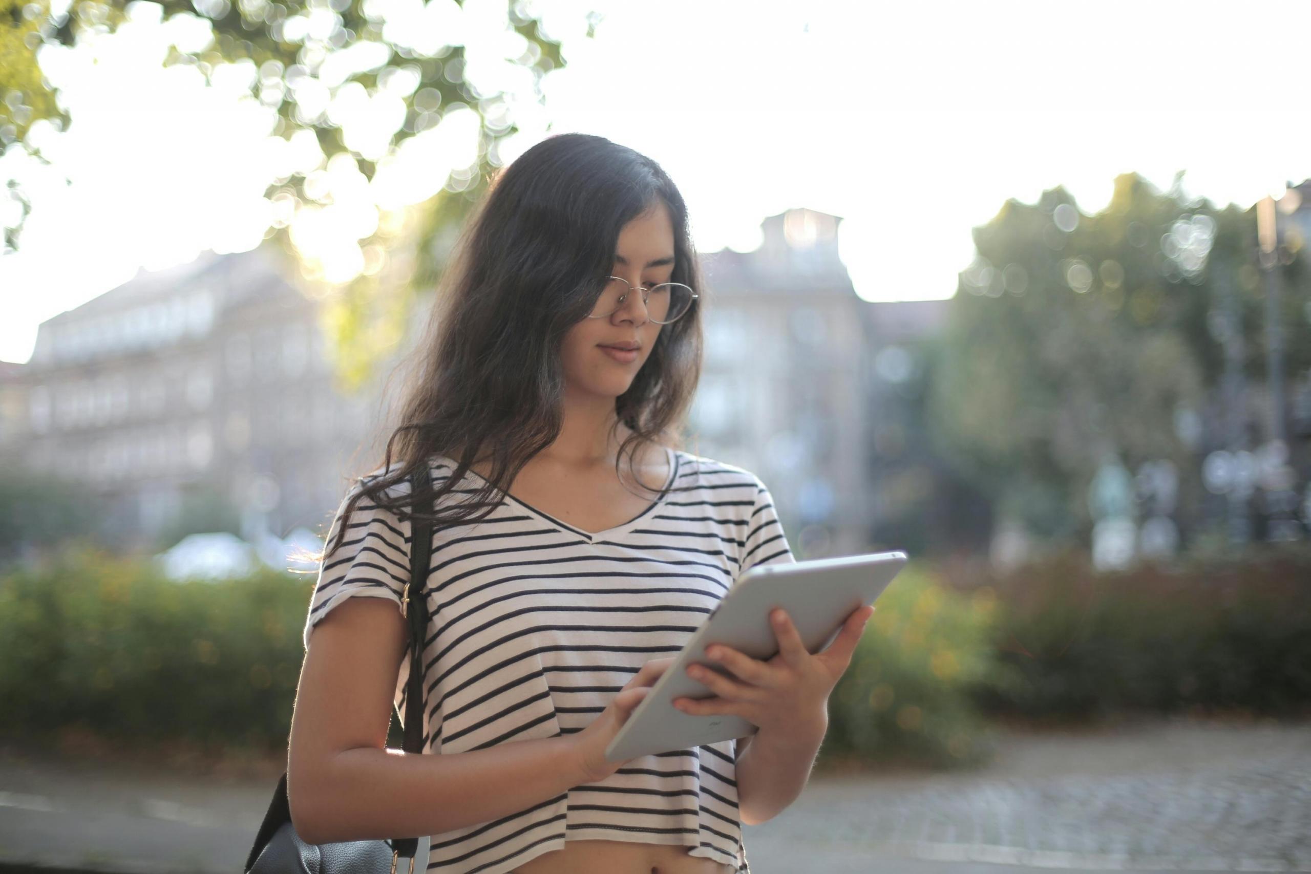 Een vrouw leest op een tablet buiten met bomen op de achtergrond.