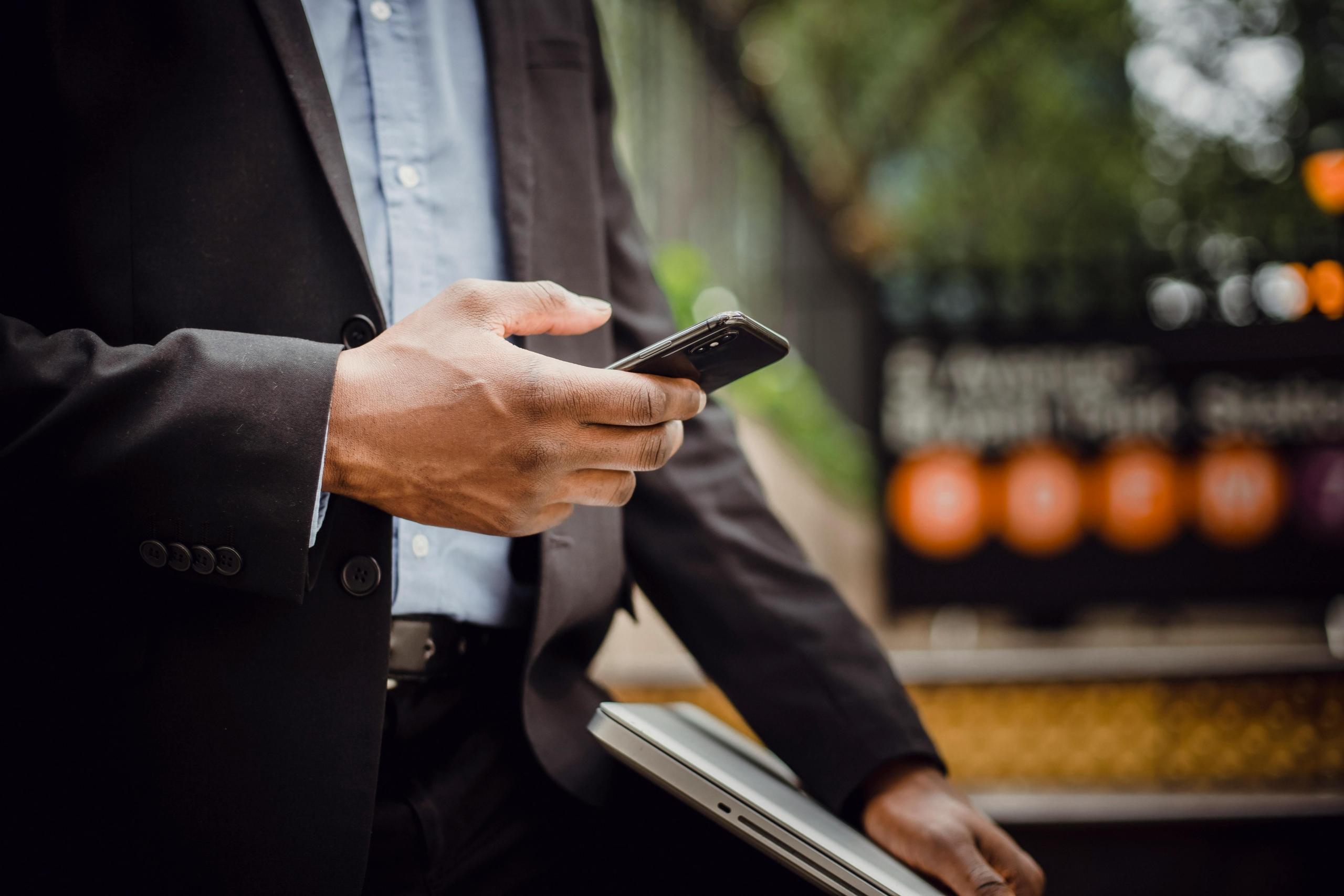 Een man in zakelijke kleding gebruikt een smartphone naast een laptop.