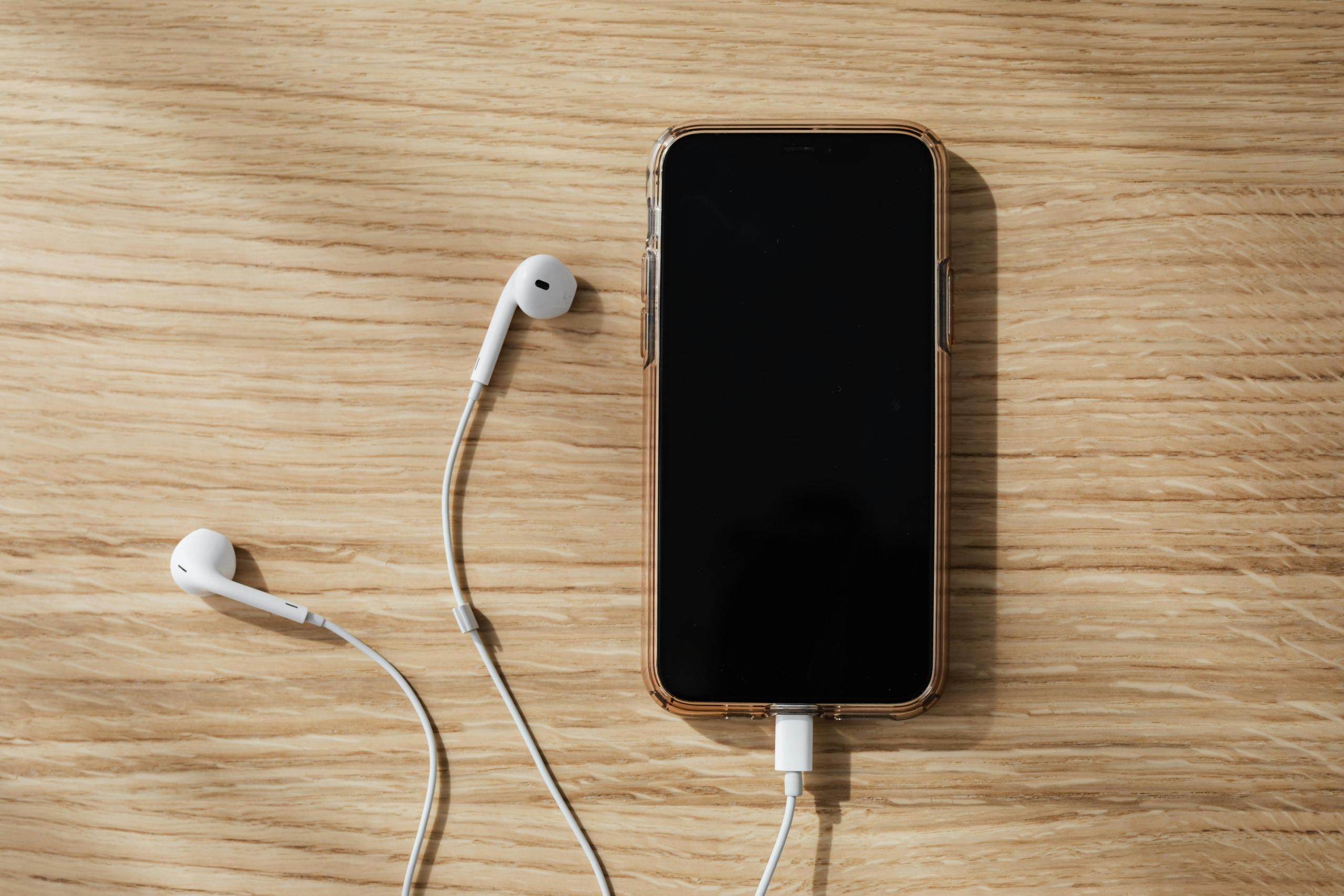 Een smartphone ligt op een houten oppervlak, aangesloten op oordopjes.
