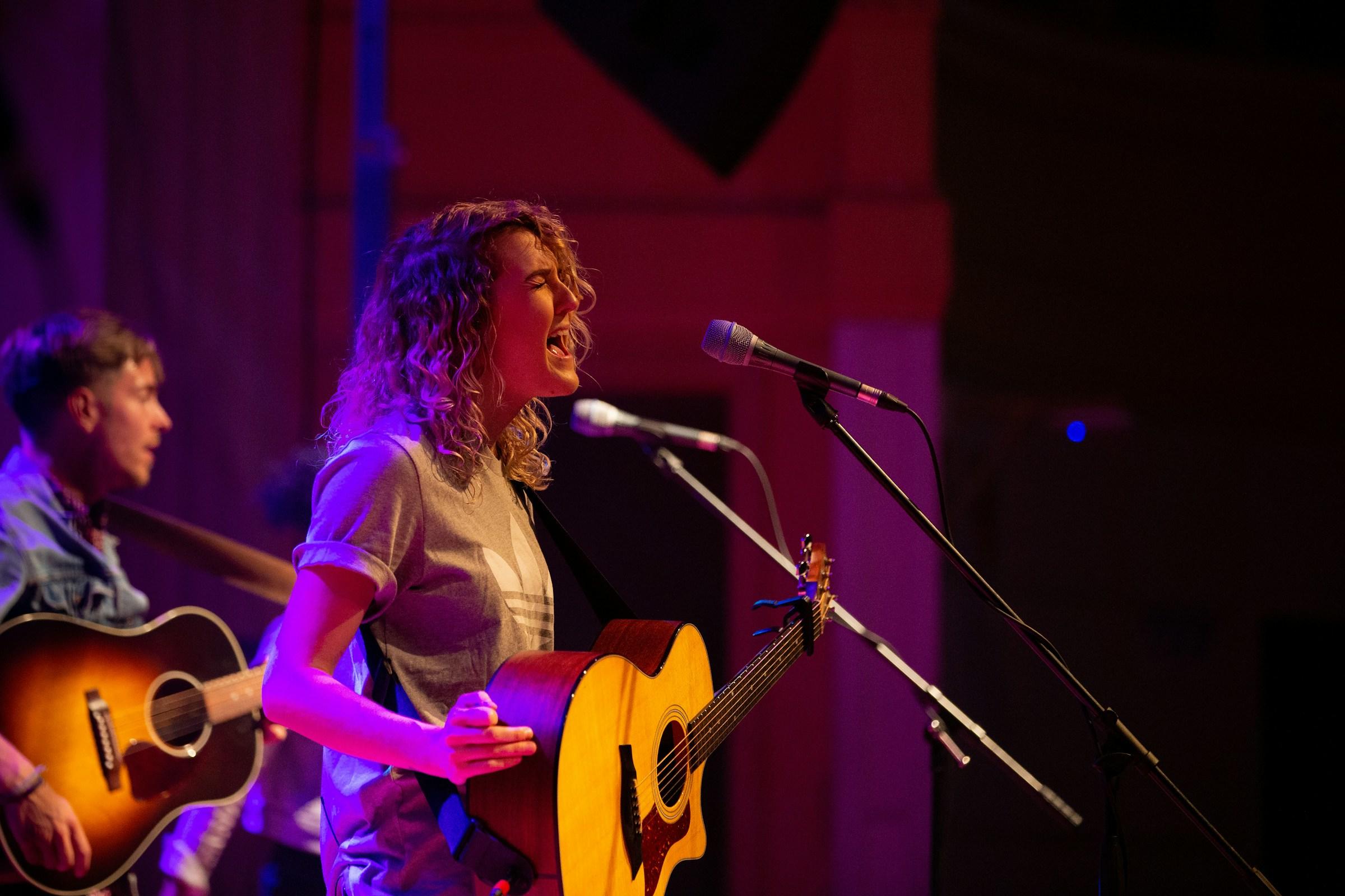Uitbundig zingende vrouw met gitaar achter microfoons