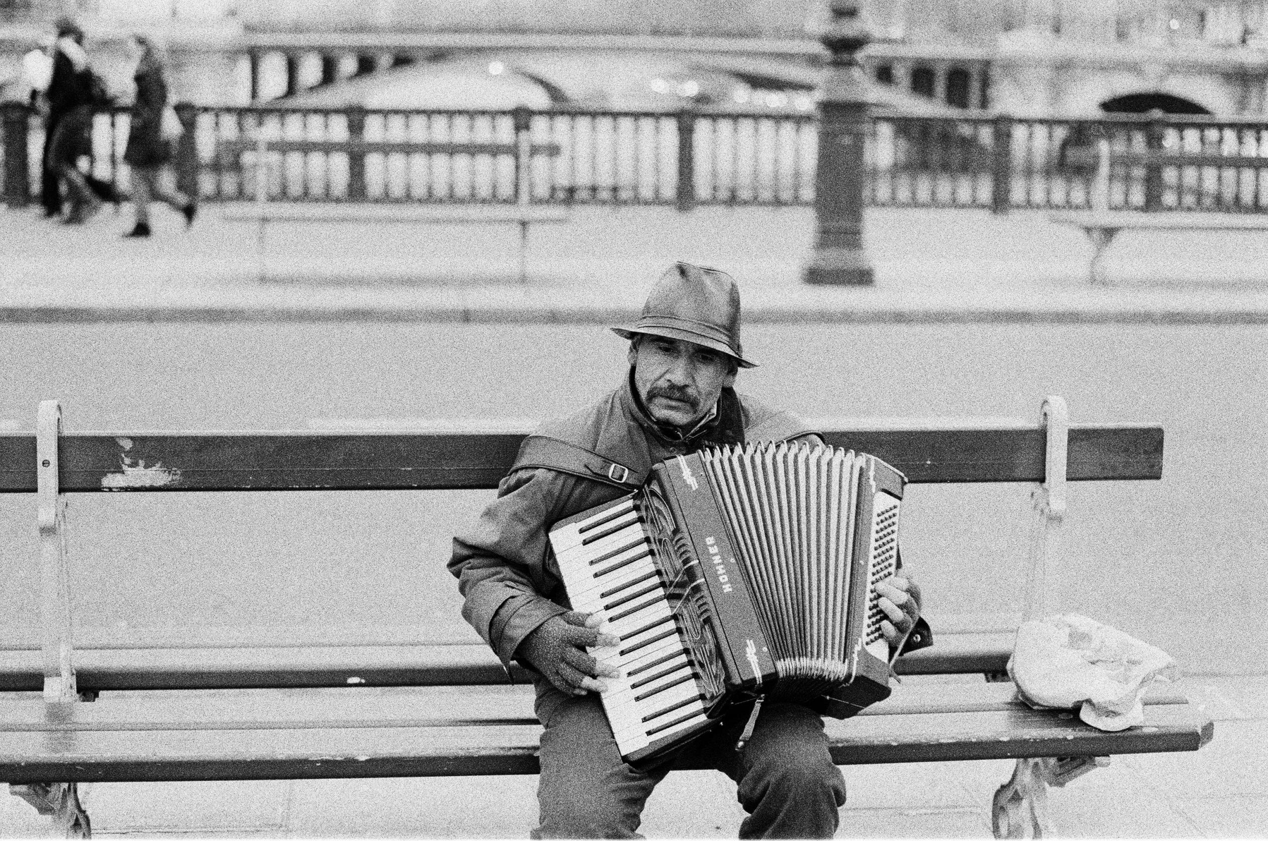 Man zit op bankje op straat en speelt accordeon.