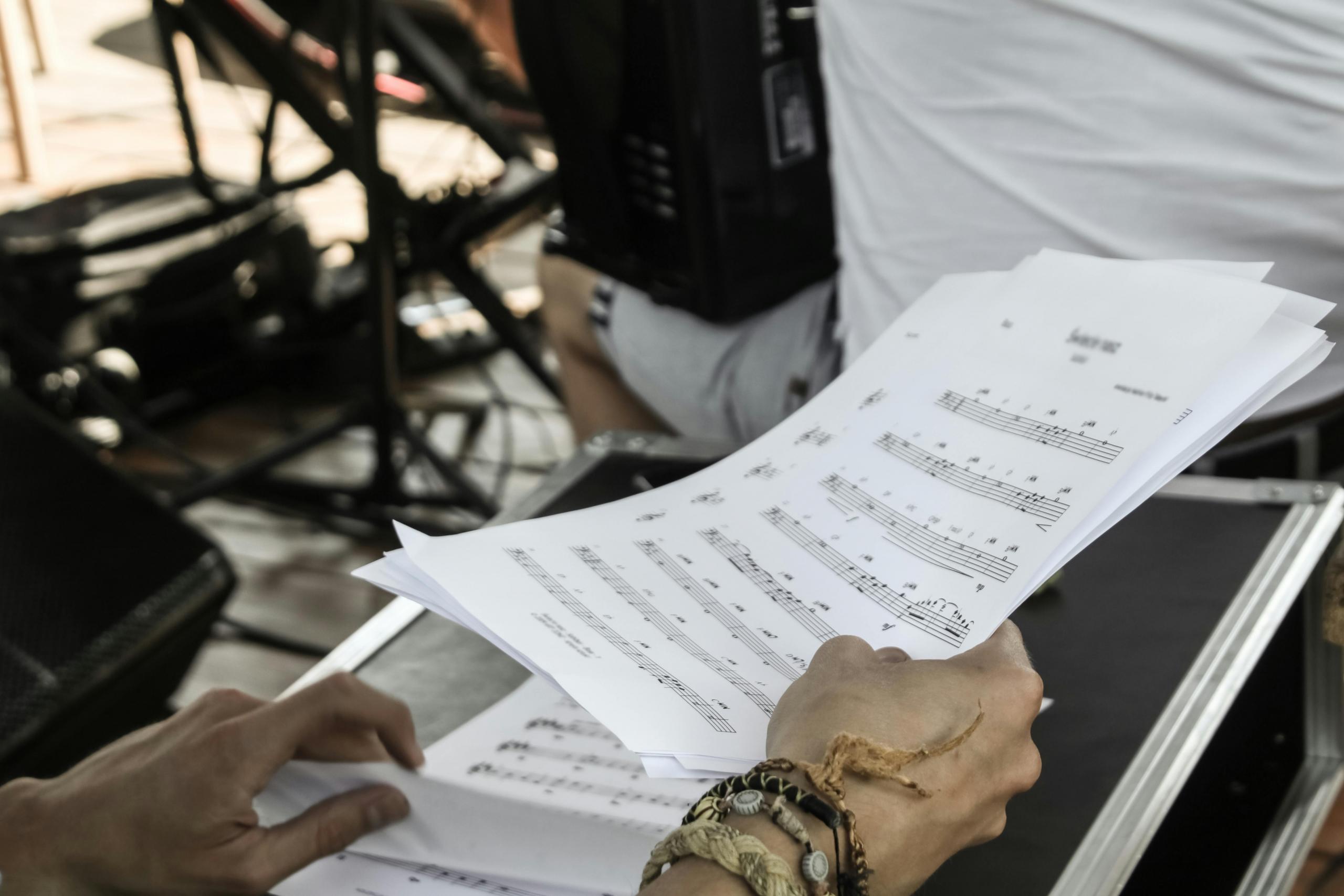 Handen die bladmuziek vasthouden met een onscherpe achtergrond van muziekapparatuur.