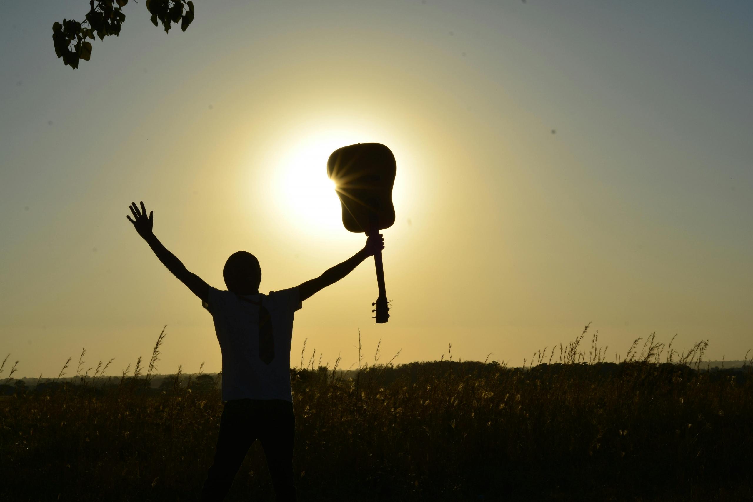 Een silhouet van een persoon die een akoestische gitaar omhoog houdt tegen een zonsondergang achtergrond.