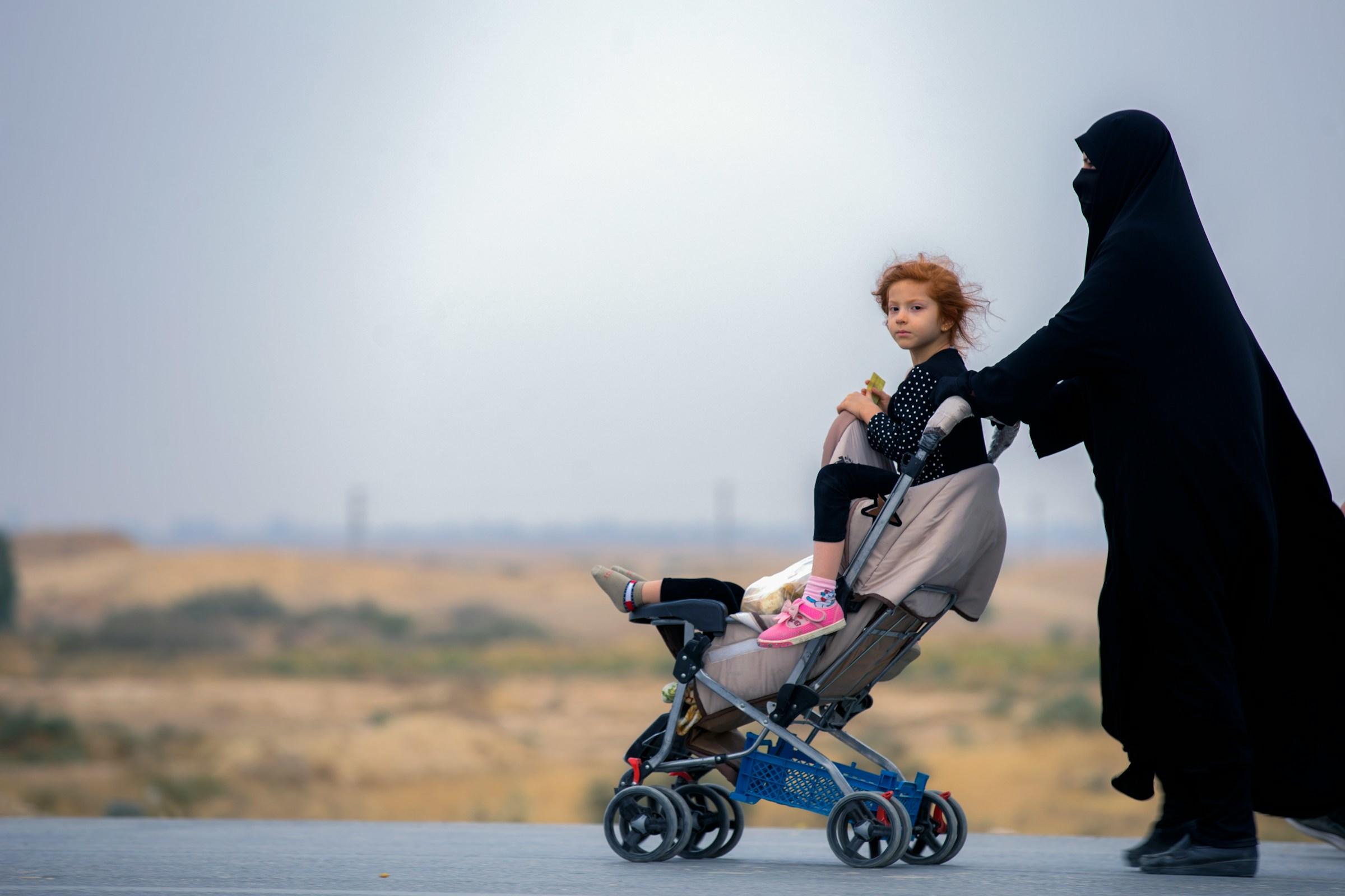 Volledig in het zwart geklede persoon duwt wandelwagen met twee kinderen