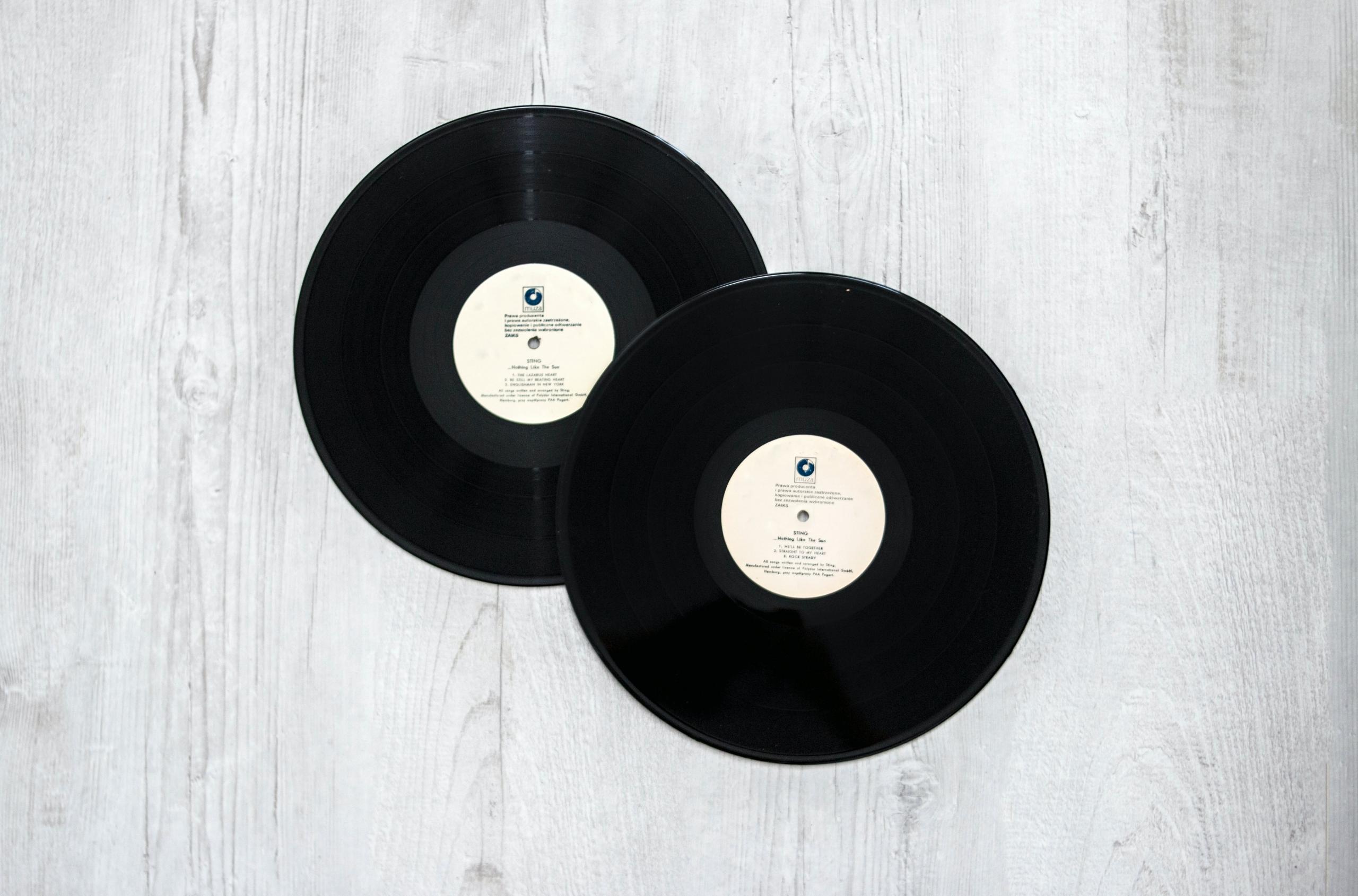 Twee zwarte vinylplaten die op een lichte houten achtergrond liggen.
