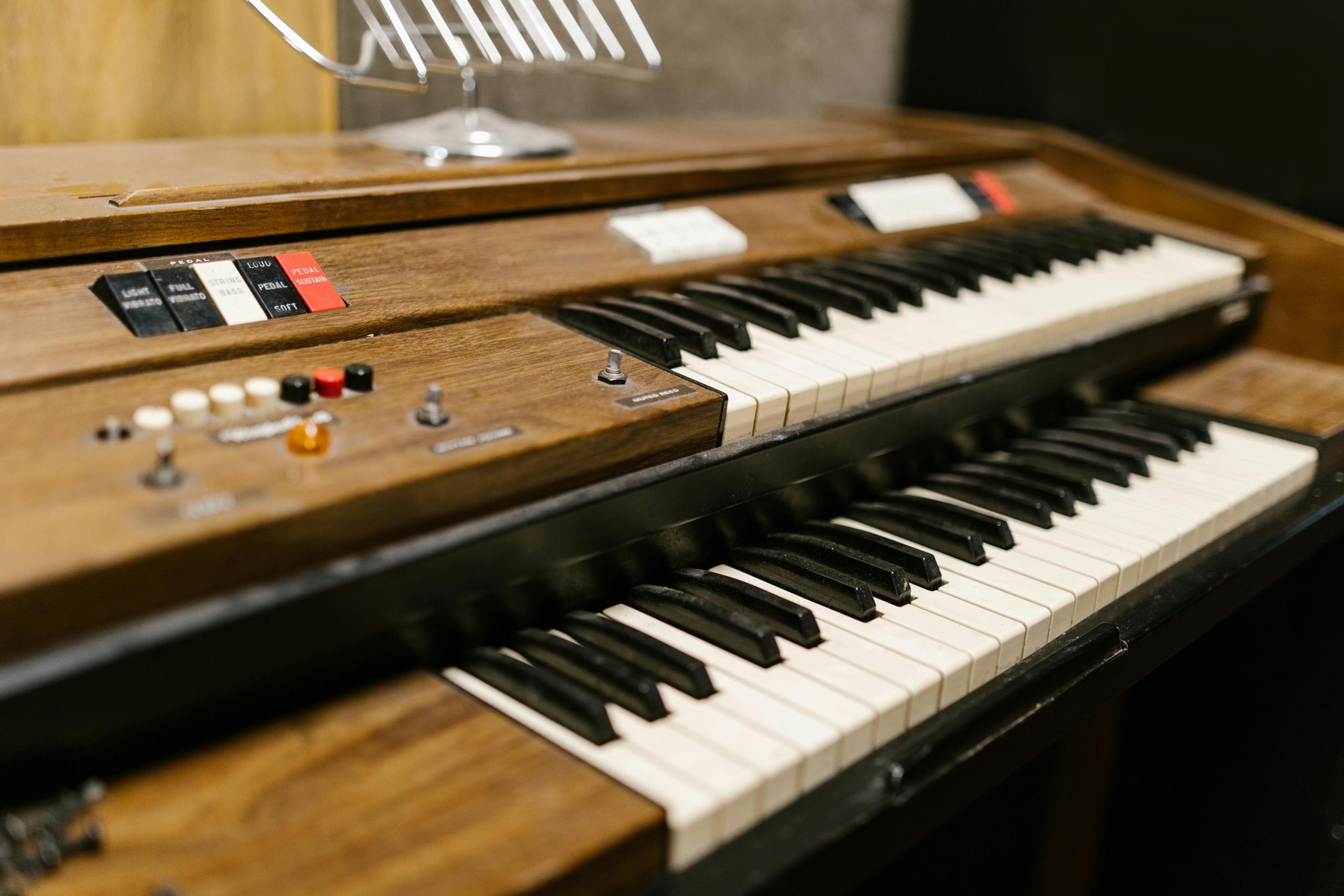 Een close-up van een houten elektronisch orgel met twee klavieren en diverse schakelaars en knoppen.