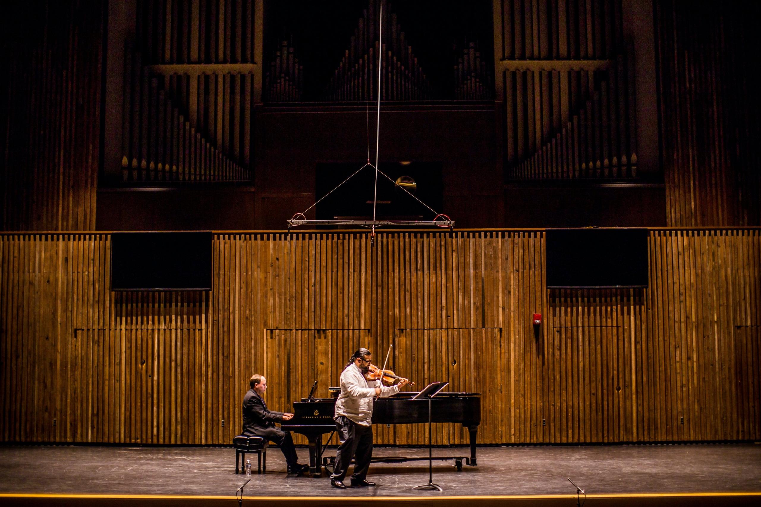 Een piano met een pianist en een violist die zich voorbereiden of oefenen op het podium.