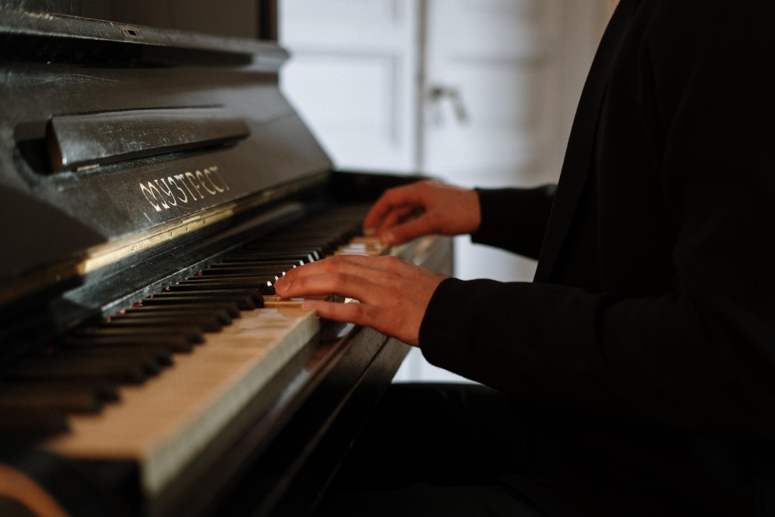 Een persoon speelt op een oude piano, gefocust op de handen.