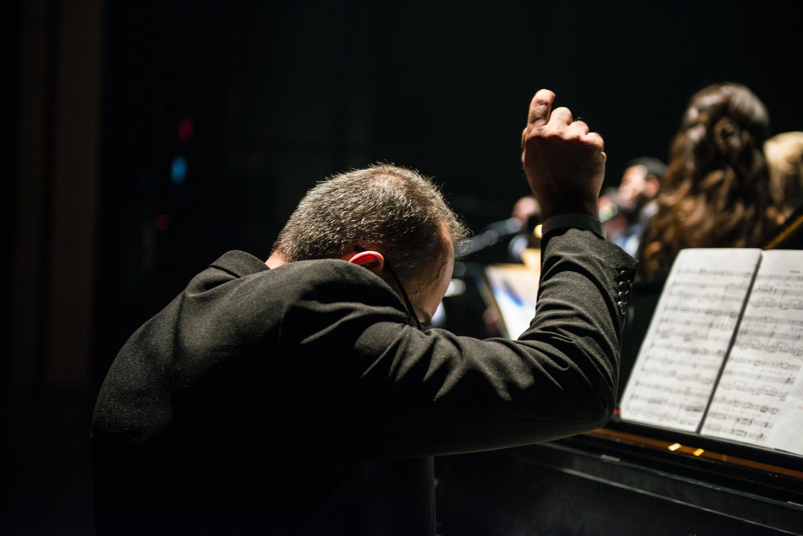 Een dirigent leidt een ensemble met een partituur op de piano.