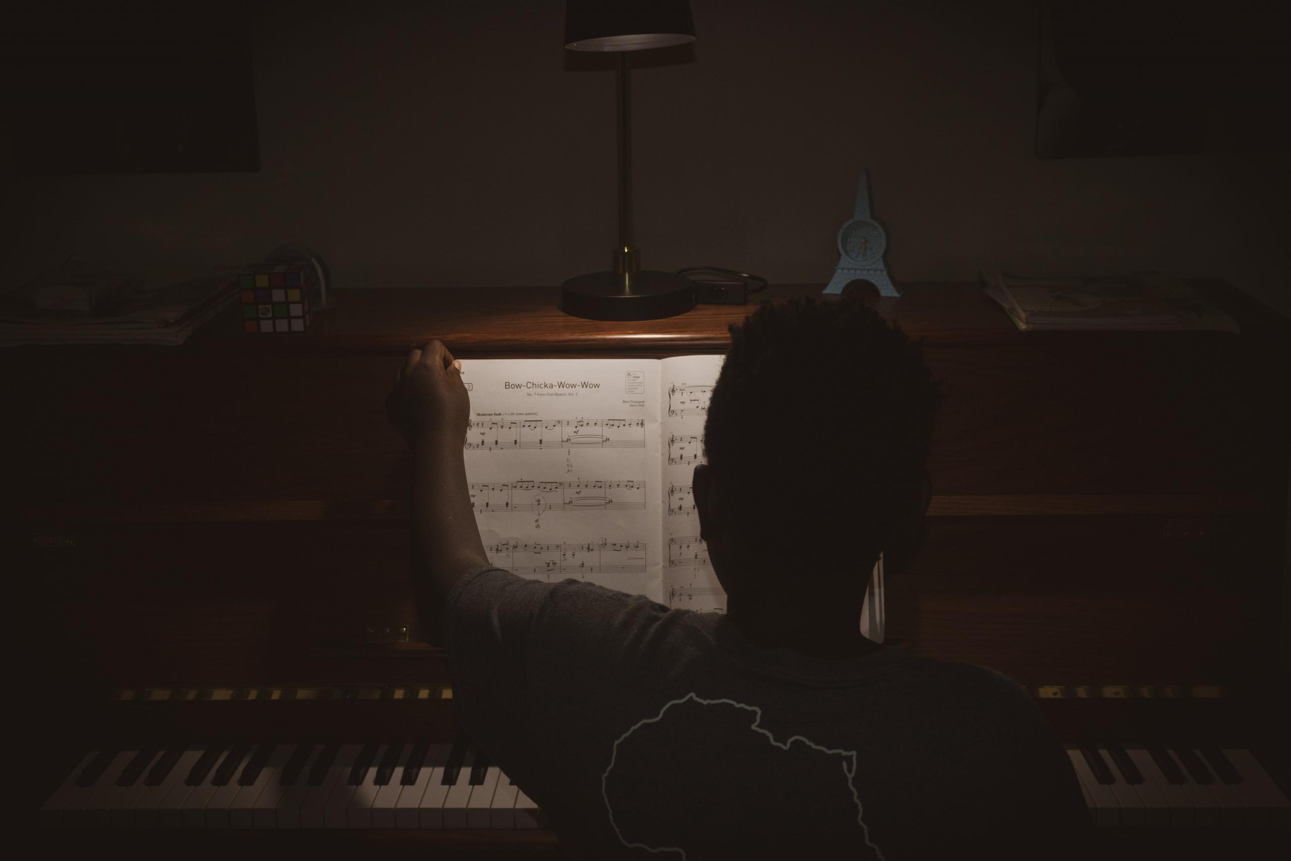 Persoon aan het piano spelen met bladmuziek onder een lamp.