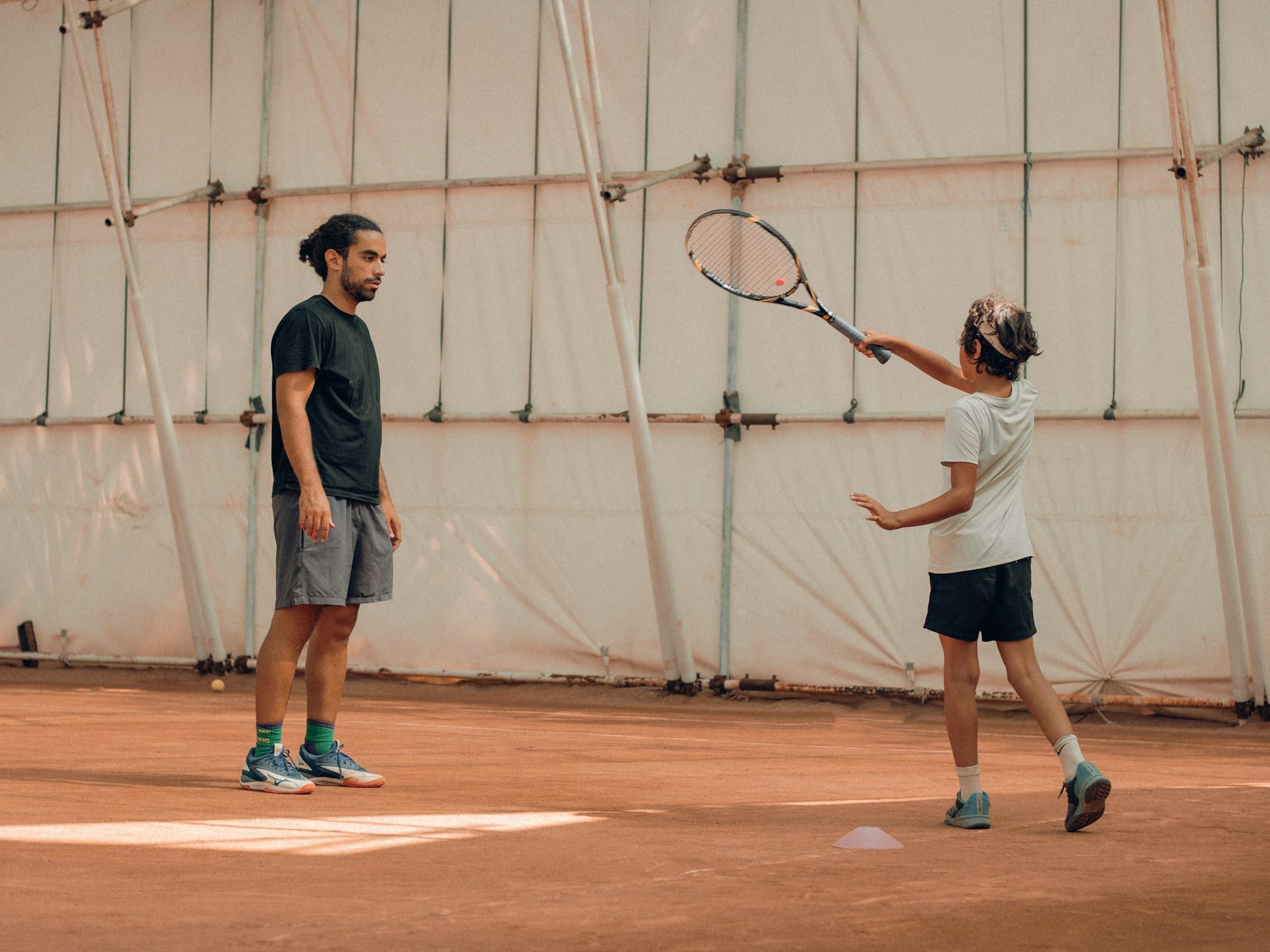 Jonge persoon met opgeheven racket in hand en toekijkende persoon