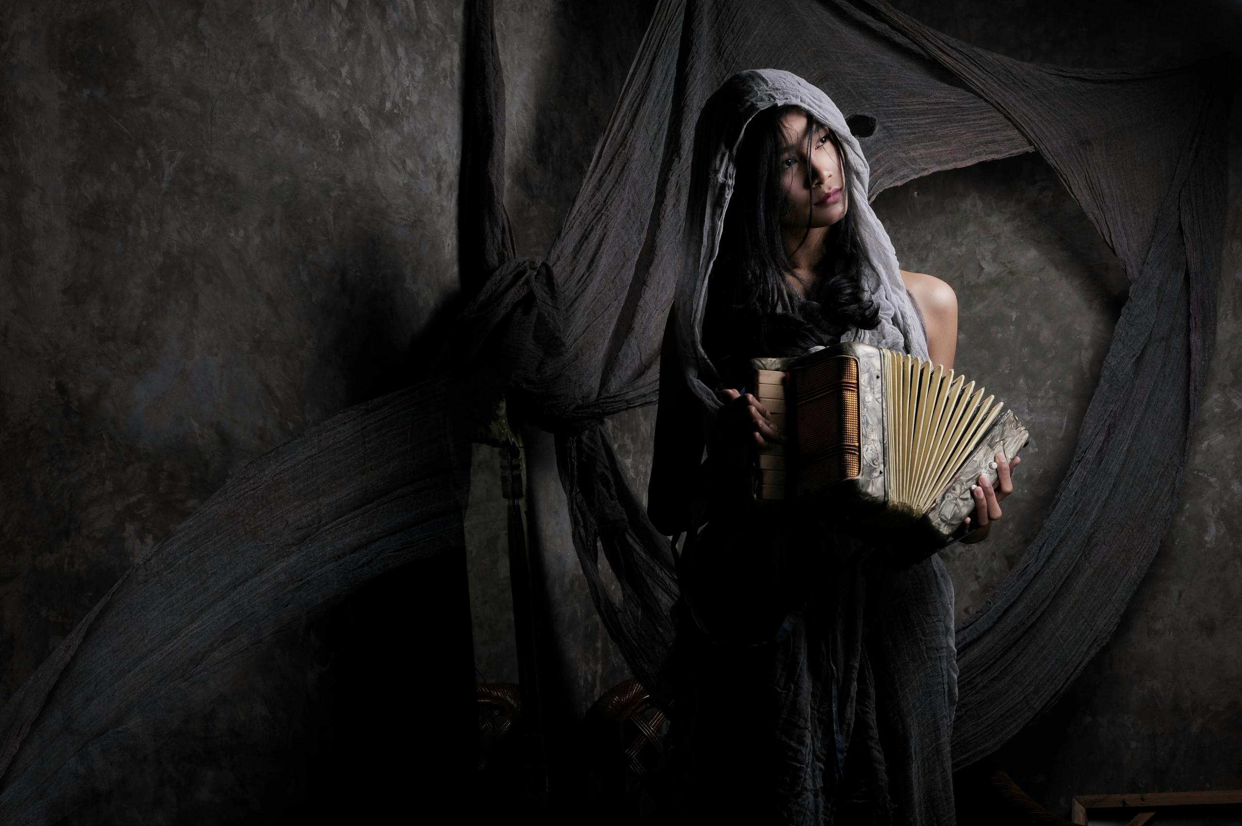 Een vrouw in een sfeervol verlichte omgeving, gehuld in grijze stoffen, die een accordeon vasthoudt.