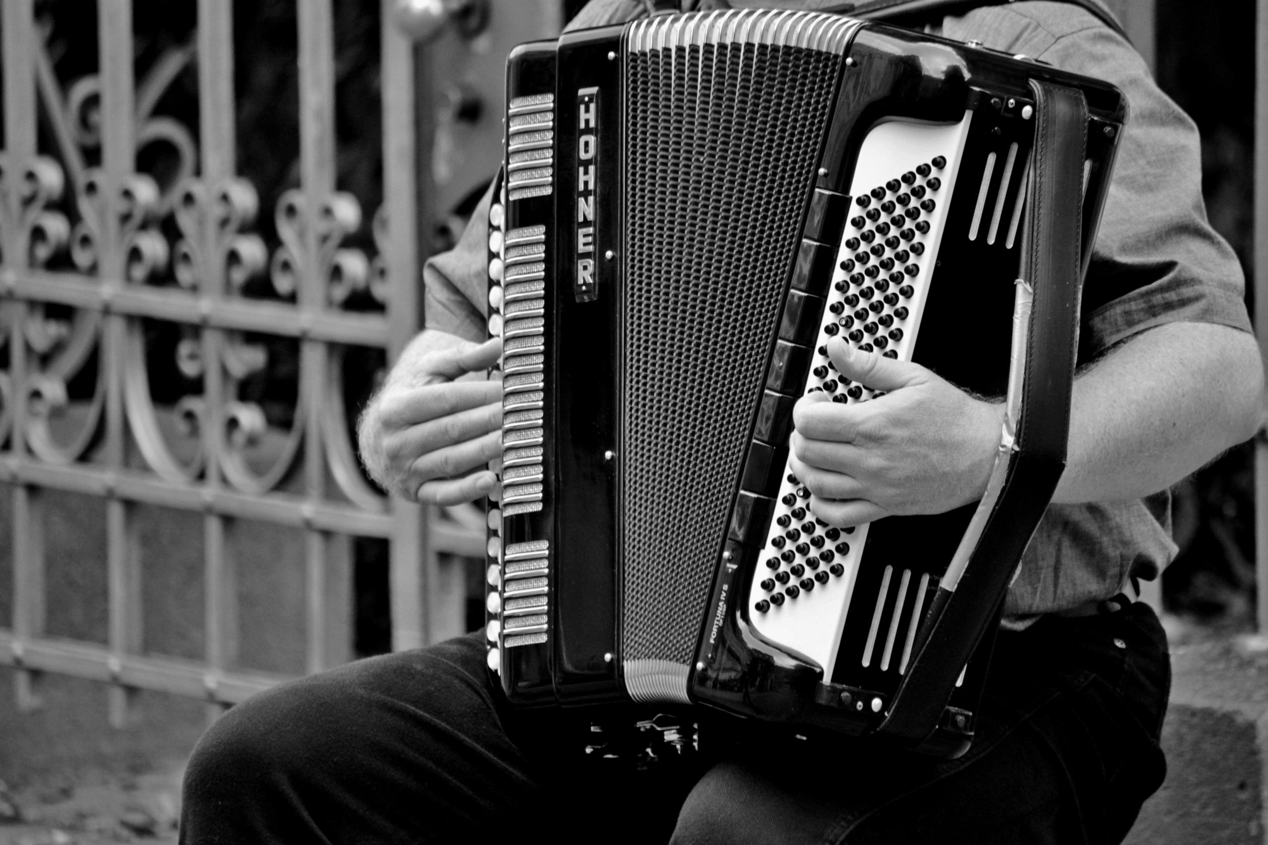 Een man in zwart-wit foto, zittend en spelend op een grote accordeon.