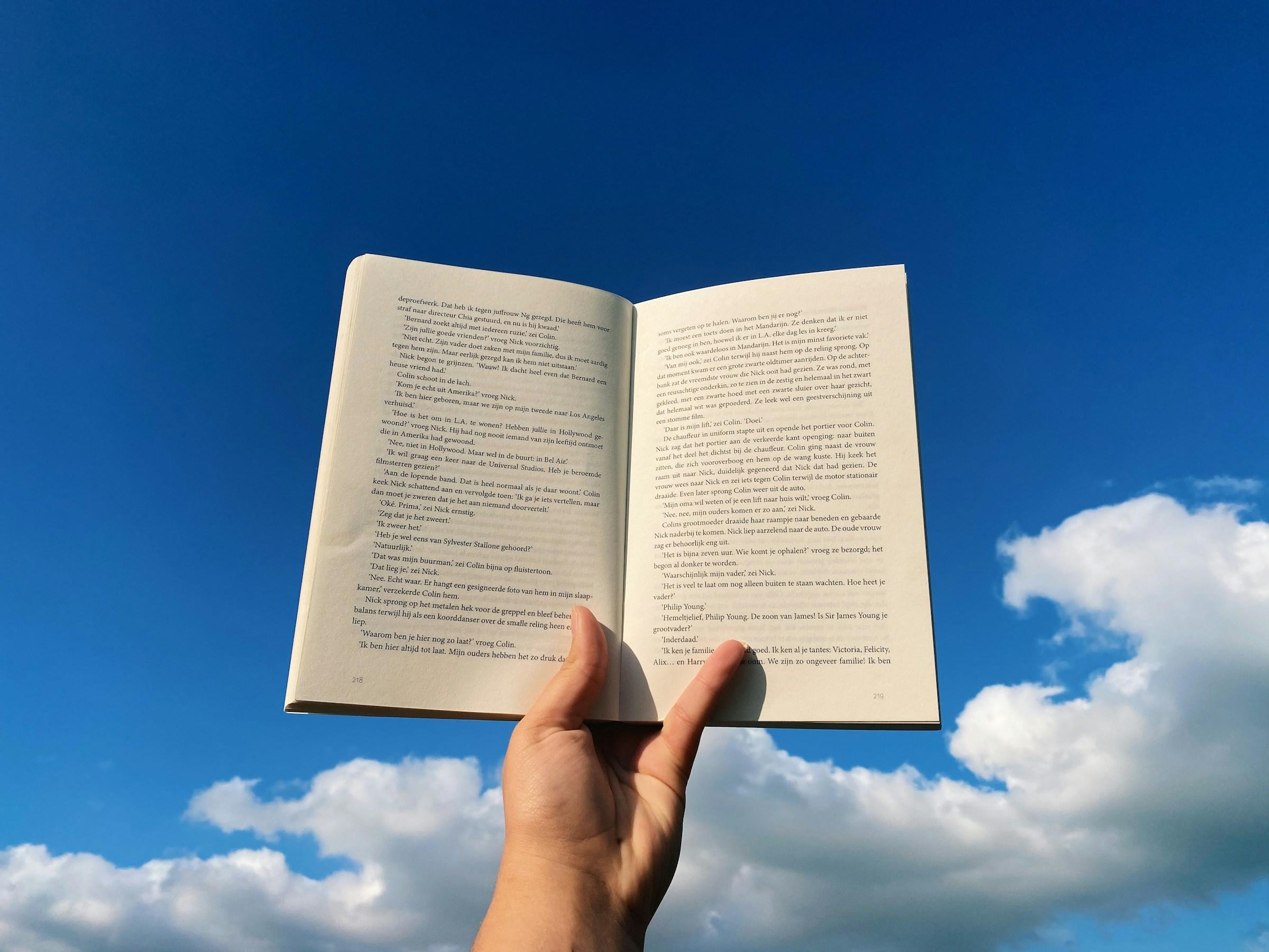 Open boek in hand tegen blauwe lucht en witte wolken